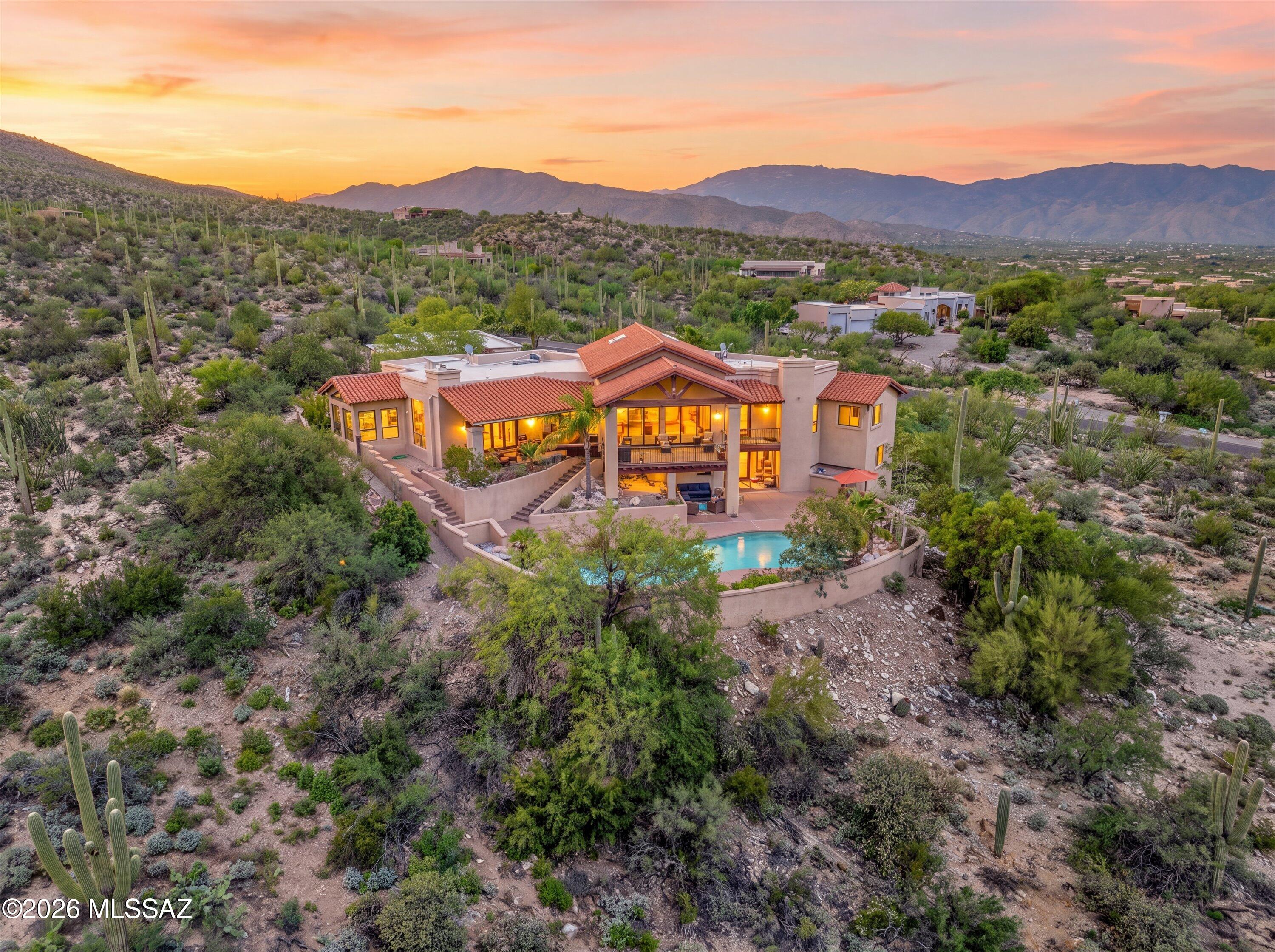 Perched high above Northeast Tucson in the Tanque Verde Valley, this gated Mediterranean Estate pairs timeless architectural character with an extraordinary hillside setting and sweeping views from Pusch Ridge to the city lights below. Approximately five bedrooms, a casita, resort-style pool, and four-car garage with workshop are set across more than two private acres of Sonoran Desert, where mature saguaros and the natural landscape create a remarkable sense of privacy and place.
Within a small, exclusive hillside community, this Estate was designed to capture a breathtaking panorama--from Vail in the southeast, across the Tucson skyline, to Pusch Ridge in the northwest, with the Santa Catalina Mountains rising directly behind the property. The elevated setting keeps the surrounding Sonoran Desert and far-reaching views at the forefront, creating a sense of seclusion high above the valley.
The chef's kitchen is designed for both cooking and entertaining, with a large center island, prep sink, professional-style gas range, double wall ovens, rich stone counters, wine refrigerator, and walk-in pantry. Just beyond, a spectacular glass-wrapped dining nook feels suspended within the Sonoran Desert, with a vaulted natural-wood ceiling, exposed beams, clerestory windows, and walls of glass framing the mountains from nearly every angle. Direct access outdoors extends the space even further, creating an unforgettable setting for morning coffee, intimate dinners, or simply taking in the changing desert light.
The home's architectural character continues throughout the main living spaces, where soaring cathedral and beamed ceilings and walls of glass frame the surrounding landscape. A gas fireplace anchors the family room, with direct access to its own patio extending the living space outdoors and showcasing the views beyond. The living room features an elegant wet bar and opens to a separate patio, further enhancing the home's effortless indoor-outdoor flow.
The primary suite is a private retreat with its own gas fireplace, generous sitting area, and dual walk-in closets. The expansive primary bath features dual vanities, a striking freestanding hammered-metal jetted soaking tub positioned to capture the surrounding views, and an oversized walk-in shower.
Two additional guest suites in the main residence each feature a private en-suite bath, offering exceptional comfort and privacy for family and overnight guests.
A casita adds exceptional flexibility with two bedrooms, a full bath, walk-in closet, fireplace-warmed living area, and kitchenette with a sunny dining nook--ideal for extended family, guests, or use as a private pool house.
Outdoor living is where this Estate truly comes into its own. The resort-style pool is framed by mature palms and desert landscaping, with the mountains rising dramatically beyond. A private courtyard, tiered patios, stone stairways, multiple covered outdoor spaces, and intimate gathering areas follow the natural hillside, creating distinct places to dine, entertain, unwind, and take in the surroundings throughout the day.
A north-side nook patio provides a secluded setting for dinner under the stars, while the back patio opens to spectacular western sunsets and the glow of Tucson's city lights each evening. During summer monsoons, the sound of rainwater rushing through the gullies below adds yet another dimension to life high above the valley.
An oversized four-car garage with dedicated workshop and half bath provides exceptional space for vehicles, hobbies, and storage. A flexible bonus room and dedicated laundry add versatility to the home's thoughtfully designed layout.
Located within the well-regarded Tanque Verde school district and just a short walk from a trailhead at the end of the street, this Estate offers a rare combination of acreage, elevation, privacy, guest accommodations, resort-style outdoor living, and unobstructed views. From the Santa Catalina Mountains rising behind the property to sweeping western sunsets and Tucson's city lights below, every element of this hillside setting speaks to what makes living in the Tanque Verde Valley so extraordinary.
This exceptional offering is proudly represented by the valley's most experienced luxury home marketing team, known for record-setting results across the greater Tucson area and a presentation standard designed specifically for estates of this caliber. For additional photography, further details, or to arrange a private showing, please reach out to experience this remarkable hillside Estate in person.