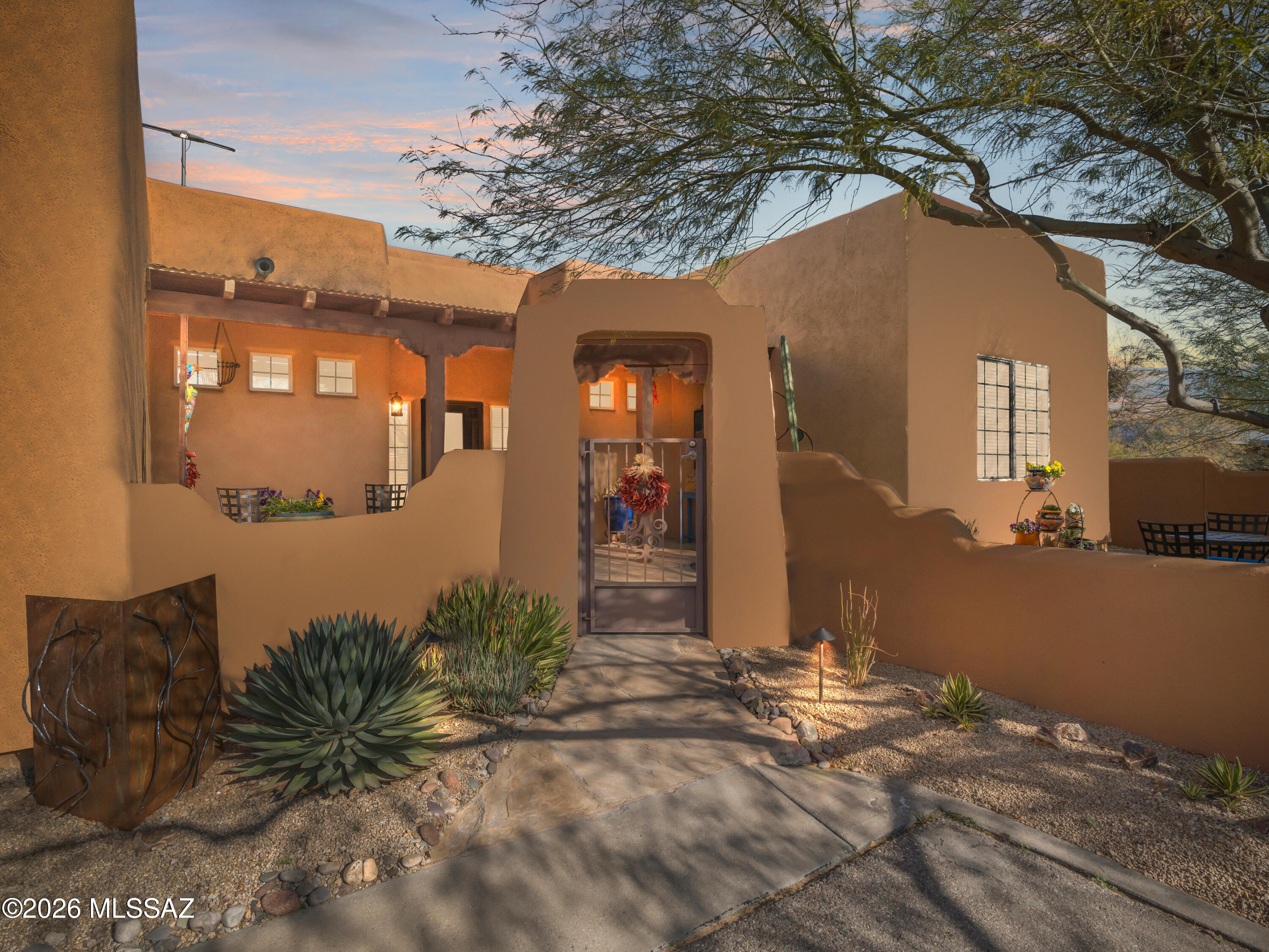 Welcome to a charming desert retreat nestled in the heart of Tucson. This beautifully designed home showcases classic Southwestern architecture with smooth stucco walls, earthy tones, and a private gated entry that creates an immediate sense of serenity and arrival. Mature desert landscaping, agave, and natural stone accents frame the walkway, perfectly complementing the surrounding Sonoran scenery. Inside, the home opens to a spacious, light-filled living area featuring soaring ceilings with exposed wood beams, tile flooring, and a cozy fireplace that anchors the space. The open-concept layout flows seamlessly into the kitchen and dining areas, making it ideal for both everyday living and entertaining. Warm wood cabinetry, generous counter space, and thoughtfully placed lighting add to the home's inviting ambiance. Large windows and glass doors invite natural light while offering tranquil views and easy access to the outdoors. Thoughtful design details throughout reflect comfort, character, and timeless appeal. Whether relaxing indoors or enjoying peaceful desert evenings on the rooftop, this home offers a perfect blend of privacy, style, and Southwestern charm. Conveniently located in a desirable Civano neighborhood, this property offers a unique opportunity to enjoy authentic desert living with comfort and elegance.
