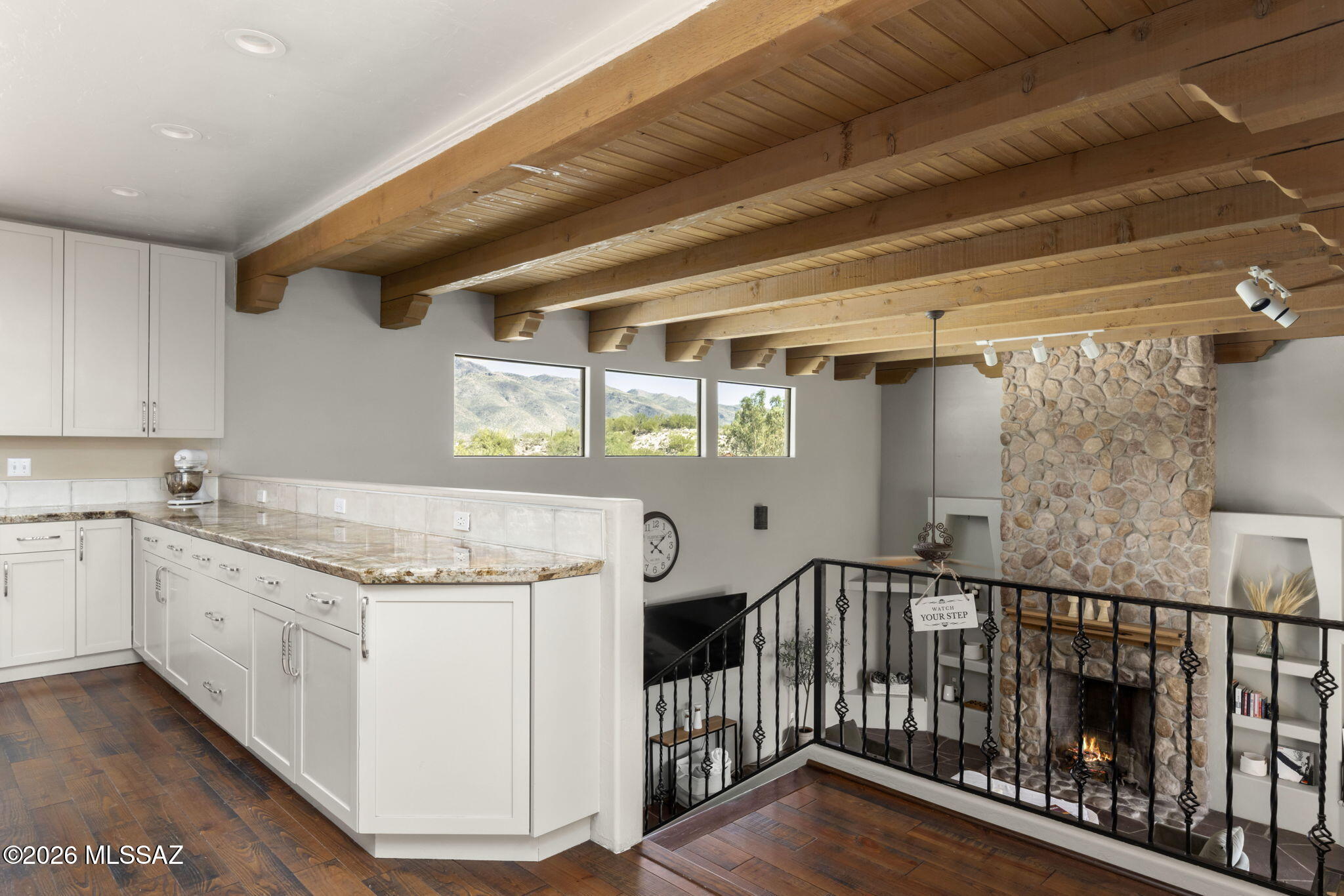 Architectural Character, Dramatic Views & a Distinctive Foothills Setting. Set within gated Rockcliff near Sabino Canyon, this custom home, designed by David Bushell, is defined by its architecture and remarkable Catalina Mountain, desert & city-light views. Soaring wood-beamed ceilings, handcrafted wood doors, organic wood and flagstone flooring, and windows thoughtfully positioned toward the surrounding landscape create a home with unmistakable Southwestern character. The open kitchen faces the Catalinas and features floor-to-ceiling cabinetry, granite countertops, an induction cooktop beneath a striking decorative copper hood, & a substantial island with seating for six. Two generous living areas offer flexibility, including a dramatic family room with a floor-to-ceiling stone fireplace flanked by built-in display shelves and glass doors opening to a covered patio and courtyard overlooking the city lights.
The primary suite includes a corner fireplace, patio access and an updated bath with stained concrete floors, walk-in rain shower and jetted tub. Each bedroom has a walk-in closet, while separate guest quarters with a full bath also work beautifully as a private office or studio.
Outdoor spaces are equally memorable. The covered rear patio overlooks a private backyard with an iron view fence preserving the mountain and desert outlook. A movable deck cleverly conceals an above-ground pool or provides additional deck space, and all metal garden beds convey. Above the approximately 30-foot-deep garage, a rooftop deck offers an extraordinary vantage point for sunsets, stargazing, monsoon storms, Catalina Mountain views and Tucson city lights.
A truly distinctive Rockcliff property, close to Sabino Canyon, Canyon Ranch, shopping, dining and nearby bike paths. View the lifestyle video for another perspective on the property!