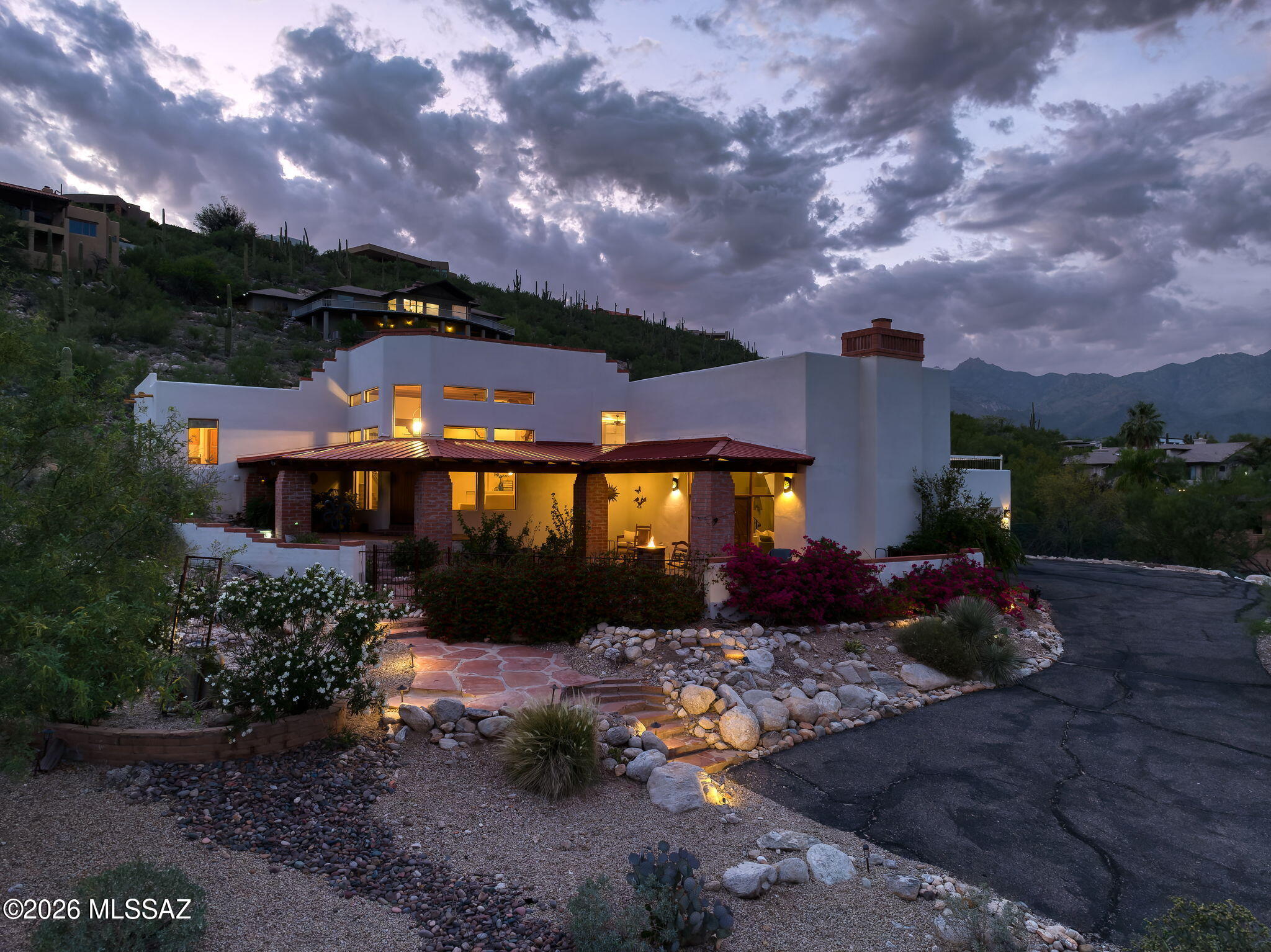 $20,000 SELLER CREDIT + DISTINCTIVE FOOTHILLS ARCHITECTURE & VIEWS! Seller is offering a $20,000 credit toward replacement of the home's polybutylene piping, although the sellers report no history of plumbing issues.
Set within gated Rockcliff near Sabino Canyon, this custom home designed by David Bushell is defined by its architecture, privacy and remarkable Catalina Mountain, desert and city-light views. Soaring wood-beamed ceilings, handcrafted wood doors, wood and flagstone flooring, and windows intentionally positioned toward the surrounding landscape give the home unmistakable Southwestern character.
The kitchen looks directly toward the Catalinas and features floor-to-ceiling cabinetry, granite countertops, an induction cooktop beneath a decorative copper hood & a substantial isla with seating for six. Two generous living areas provide flexibility, including a dramatic family room anchored by a floor-to-ceiling stone fireplace with built-in display shelving. Glass doors open to the covered front patio and courtyard, where Tucson city lights become the evening backdrop. The primary suite includes a corner fireplace, patio access and an updated bath with stained concrete floors, walk-in rain shower and jetted tub. Each bedroom offers a walk-in closet. Separate guest quarters with a full bath provide additional flexibility as a private office, studio or guest retreat.
Outdoor spaces take full advantage of the setting. The covered rear patio overlooks a private backyard enclosed by an iron view fence that preserves the mountain and desert outlook. A movable deck can serve as additional outdoor space or open to reveal the above-ground pool beneath; metal garden beds convey.
Above the approximately 30-foot-deep garage, a rooftop deck offers one of the home's most memorable vantage points for Catalina Mountain views, sunsets, stargazing, monsoon storms and Tucson city lights.A distinctive Rockcliff property close to Sabino Canyon, Canyon Ranch, shopping, dining and nearby bike paths. View the lifestyle video for another perspective on this special Foothills home.