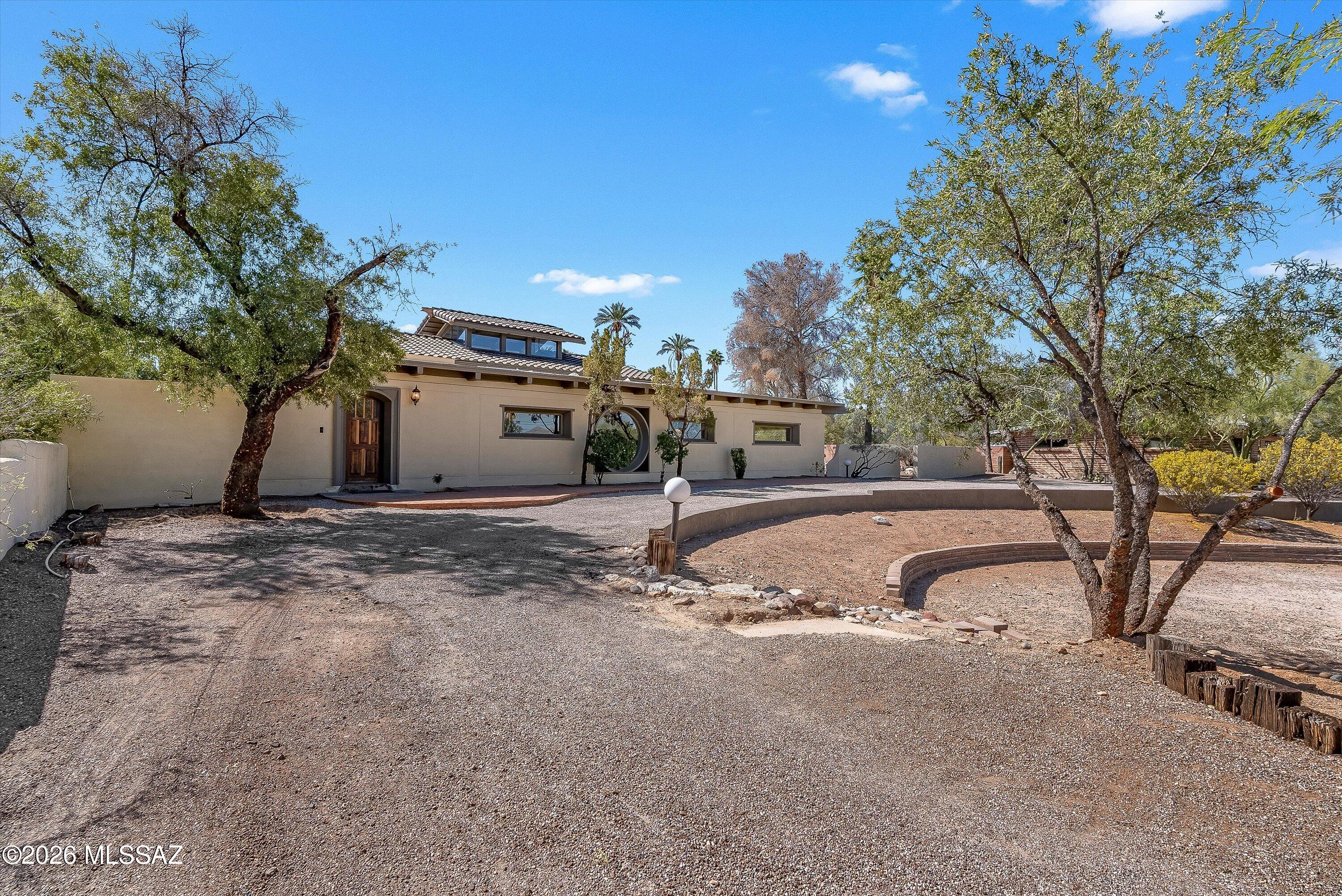 Architecturally striking desert retreat in the historic community of Harold Bell Wright Estates, featuring dramatic round windows, handcrafted woodwork, and a raised central pavilion. This one-of-a-kind residence blends bold design with artisan craftsmanship, creating a home that feels both inspiring and welcoming.
At the heart of the home, the elevated central living space is highlighted by a stunning 6-foot circular window that frames Catalina Mountain views to the north, bringing natural light and a striking architectural focal point to the room. Additional upper windows above the pavilion draw in even more daylight, enhancing the openness and dramatic design of the space.
Hand-carved woodwork throughout adds warmth and character, showcasing the craftsmanship that defines the home. The flexible layout includes two primary suites and two guest bedrooms, each with their own exterior entrances--ideal for hosting guests, multigenerational living, or creating a private retreat-style environment.

The kitchen features stainless steel appliances, cherry cabinetry, and a generous island that offers ample workspace and gathering area. Flooring throughout the home includes a thoughtful blend of oak and pine wood floors, Saltillo tile, and mesquite wood tile, each complementing the home's distinctive architectural style.

A rare opportunity to own a private desert sanctuary where architecture, craftsmanship, and Catalina Mountain views come together.