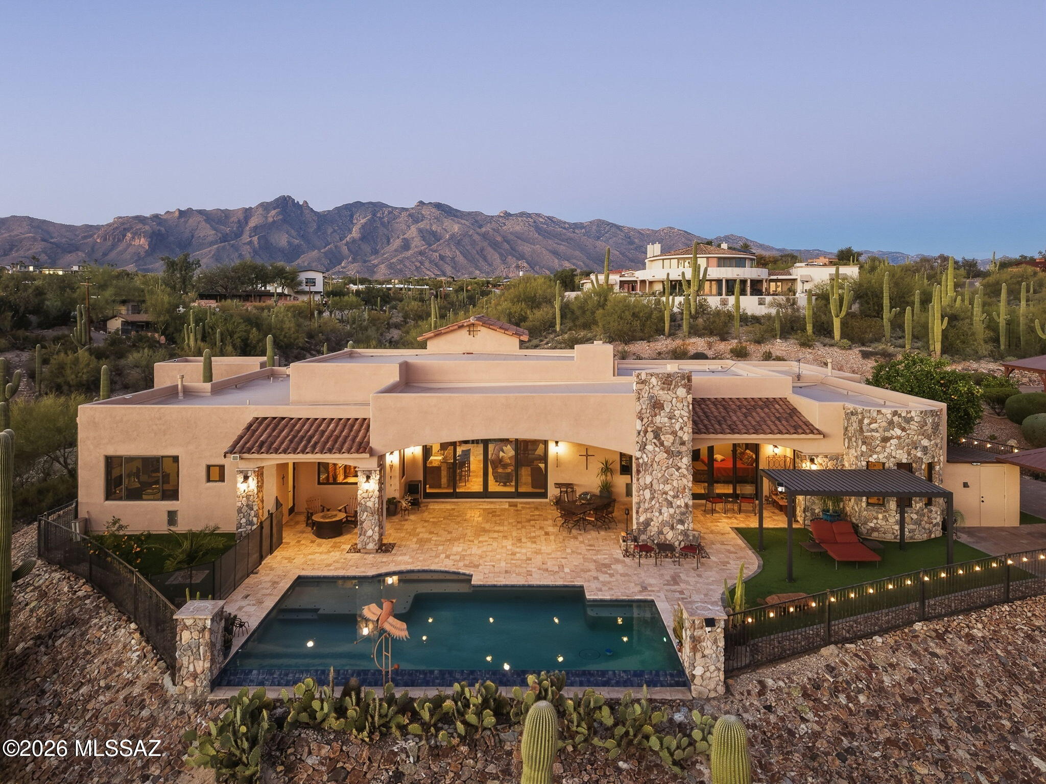 Breathtaking Foothills Estate with Panoramic City & Mountain Views-Head up the hill along the custom detailed paver and stone entry to this stunning modern Tuscan-style estate, perfectly positioned high in the Catalina Foothills to capture breathtaking panoramic views of the city lights and surrounding mountain ranges.
This elegant 4-bedroom, 3.5-bathroom residence showcases luxury and refined finishes throughout. From the rich tumbled travertine flooring to the dramatic 13-foot soaring barrel-vault ceilings, every detail was thoughtfully designed. Expansive custom windows frame the spectacular desert and city views, bringing the beauty of the outdoors into nearly every room. The heart of the home is a chef's dream kitchen featuring an impressive 10-foot oversized island, custom granite countertops, and premium Thermador appliances. The kitchen flows seamlessly into the spacious great room, highlighted by a floor-to-ceiling stone fireplace, built-in ceiling speakers/audio, and a dramatic floor-to-ceiling sliding glass wall that fully opens to blend indoor and outdoor living.
The thoughtfully designed split floor plan offers exceptional privacy, with the primary suite occupying its own private wing of the home. This oversized retreat captures the stunning views and features sliding doors opening directly to the patio, remote-controlled window shades, and an elegant tray ceiling. The spa-inspired en-suite bathroom is beautifully appointed with a soaking tub, spacious walk-in shower, dual vanities, and an impressive 13' x 13' walk-in closet that feels like a luxury boutique dressing room.
On the opposite side of the home, you'll find three additional generously sized bedrooms. One bedroom is currently designed as a sophisticated office, complete with a custom built-in desk, breathtaking city views, and a private bathroom that also provides convenient access to the pool area. The remaining two oversized bedrooms share a well-designed Jack-and-Jill bathroom and feature matching cedar-lined walk-in closets.
Step outside to an expansive covered patio finished in the same timeless travertine stone that flows throughout the home. This outdoor living space is designed for both relaxation and entertaining, highlighted by a beautiful gas-fueled stone fireplace and a designated space for outdoor television viewing. The resort-style backyard features a stunning negative-edge Pebble sheen pool with a shallow lagoon area perfect for lounging in the water while taking in the unforgettable sunset views.
The grounds are thoughtfully landscaped with lush turf, mature desert vegetation, fruit trees, and approximately 40+ mature saguaro cacti that beautifully frame the property, offering natural desert beauty with low maintenance. On the east side of the yard, a fully equipped outdoor kitchen awaits, complete with a built-in grill, smoker, cooktop, sink, and prep area--all perfectly positioned to enjoy some of the best views the property has to offer.
Car enthusiasts and hobbyists will appreciate the spacious three-car attached garage featuring a five-star dog washing station, additional storage closet, and extra-deep bays that easily accommodate a full-size truck with room to spare. As an added bonus, the property includes a detached single-car garage on the west side of the home, complete with its own private deck that captures additional mountain views and provides a unique outdoor retreat.
This one-of-a-kind Tucson property offers exceptional indoor-outdoor living, breathtaking views from nearly every space, and outstanding entertaining opportunities. With no HOA and located on a quiet no-outlet street, this home provides the perfect blend of privacy, luxury, and Foothills living.
