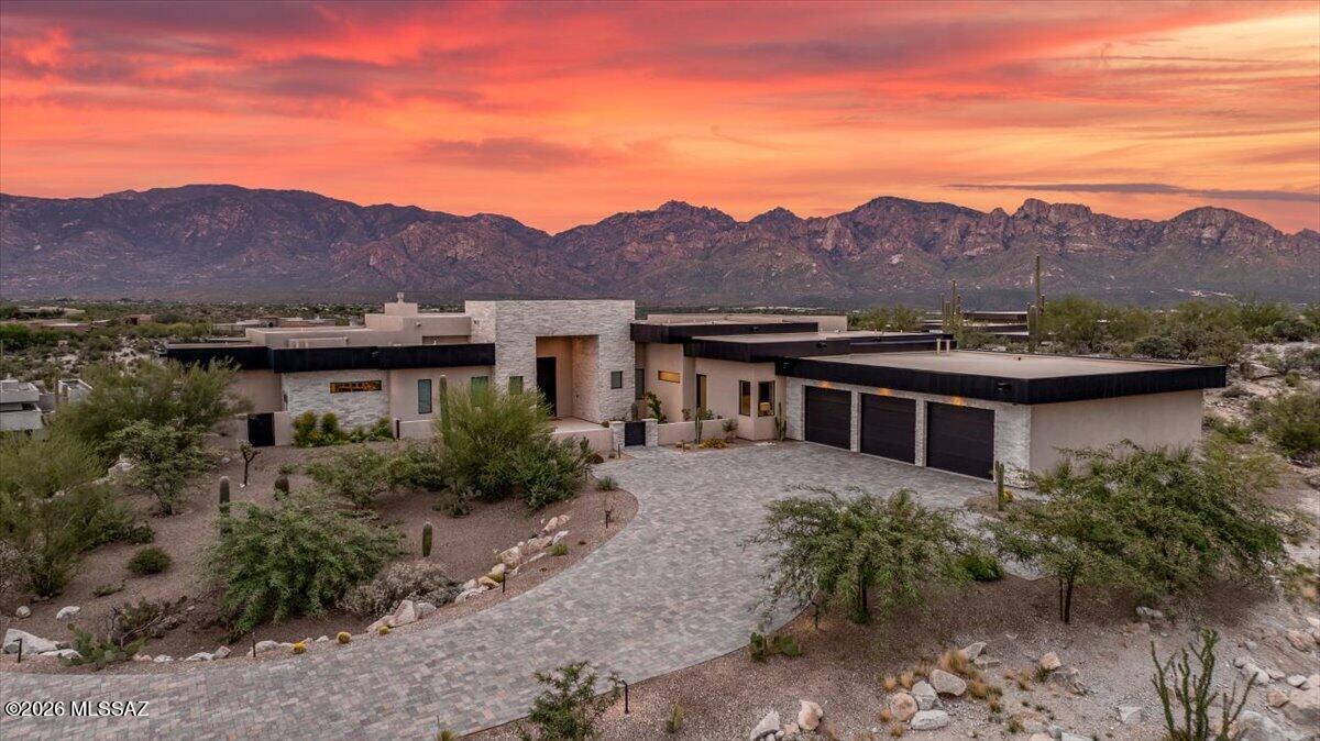 Set on an exceptionally elevated homesite in Stone Canyon, this thoughtfully designed residence captures unobstructed, edge-to-edge views of the Catalina Mountains from the rear  and Tortolita Mountains and sunsets from the front. With three spacious bedroom suites, four bathrooms and a dedicated office with built-in desk and bookshelves, the home combines exceptional finishes with a floor plan designed for comfortable everyday living and entertaining.
The kitchen is beautifully appointed with Taj Mahal quartzite countertops, Sub-Zero and Wolf appliances, steam oven and an oversized island featuring a four-foot workstation sink with dual faucets--an incredibly functional design when cooking or entertaining. Just beyond the kitchen is a spacious scullery with its own sink, open shelving, extensive storage and a beautiful backsplash. A separate bar includes both wine and beverage refrigeration.
The primary suite takes full advantage of the home's views and includes separate, fully customized closets. Her closet features built-in dressers and a dedicated vanity/getting-ready area.  Gorgeous accent wall of lime tile. The primary bath offers dual vanities and an oversized walk-in shower incorporating a soaking tub within the spacious wet room. Both guest suites are generously sized with private en-suite baths and walk-in closets.
The utility spaces have even been carefully considered. The laundry room offers extensive cabinetry, quartzite countertops, a utility sink and included washer and dryer. The garage features epoxy flooring, built-in cabinetry and an oversized climate-controlled storage room.
Outdoor living is centered around the home's remarkable setting. A deep covered patio provides generous shaded living space overlooking the Catalina Mountains, complemented by turf and a fire pit for gathering outdoors. When the evenings cool off the outdoor patio ceilings are equipped with Bromic Tungsten Smart Heat.  A roof deck offers another vantage point for enjoying sunsets, city lights and the surrounding desert landscape. At the front of the home, a private courtyard frames dramatic views toward the Tortolita Mountains.
The exterior is finished in Cork Spray, a durable coating particularly well suited to Arizona's climate. It provides added thermal insulation while resisting cracking, chipping and significant color fading.
With its elevated position, the home enjoys expansive views from nearly every window. A setting that allows the surrounding mountains and Sonoran Desert to become part of the architecture itself.