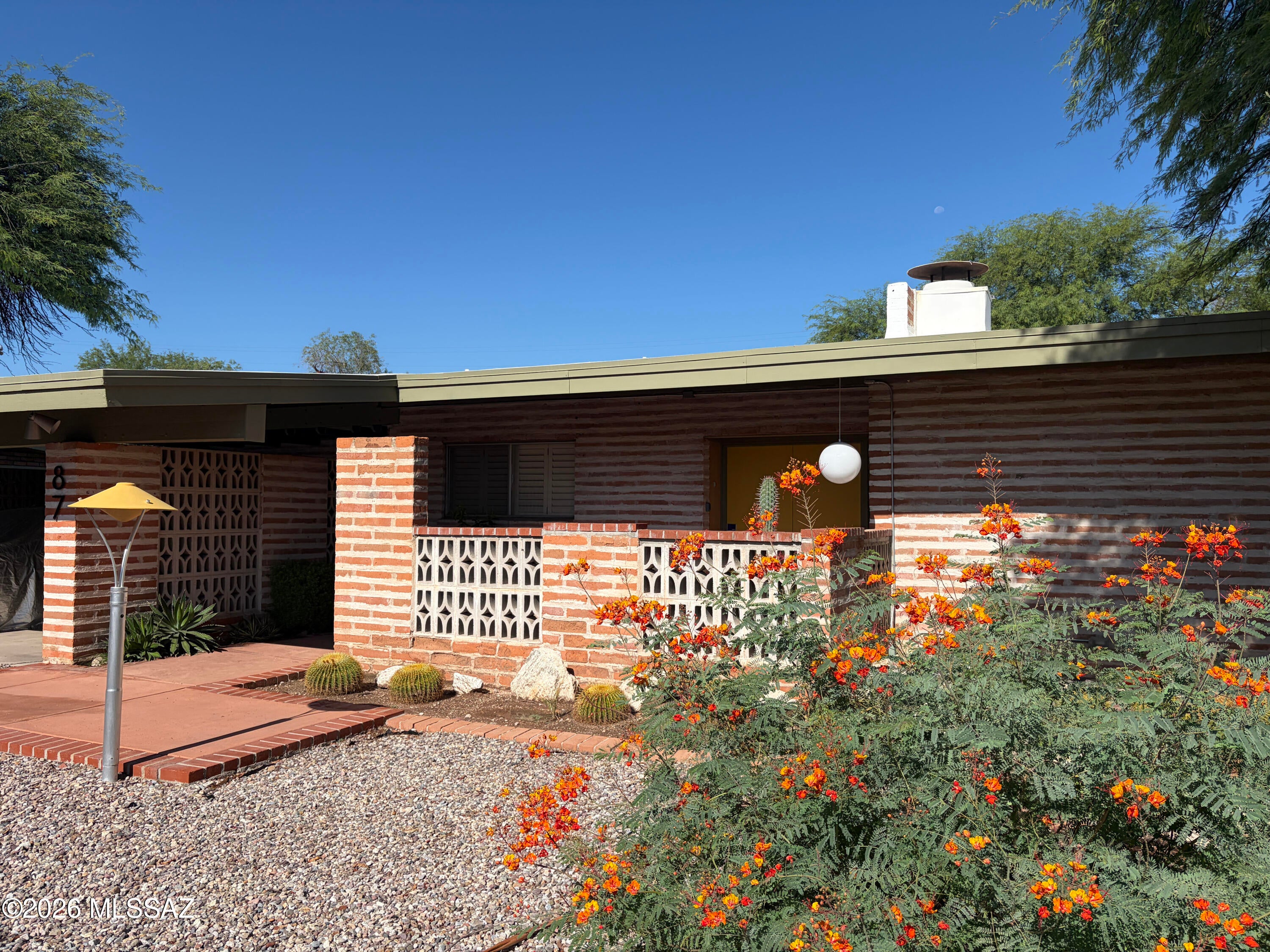 Designed by architect John Donatelli in 1963 for Edward and Kenyon Spaulding, this exceptional midcentury modern home pairs a clear modernist sensibility with materials rooted in the Sonoran Desert. Expansive windows fill the living and dining rooms with natural light, while flagstone patios extend the house into its garden setting and can be accessed from nearly every room. Thoughtfully renovated while retaining its architectural character, the property was selected for the 2023 Tucson Modernism Week home tour as a notable example of regional modern design
The home includes four bedrooms, two of which share a flexible bonus room with walls of glass, patio access, a built-in desk + a hidden closet tucked behind the bookcase. The fourth bedroom offers room for a home office, studio or den. Set on a private .36-acre corner lot, the home offers multiple outdoor living areas, mature landscaping and a terrace with a built-in bar for gathering and entertaining. Quietly tucked away near Broadway and Wilmot, this is a rare opportunity to become the next steward of a significant Tucson home.