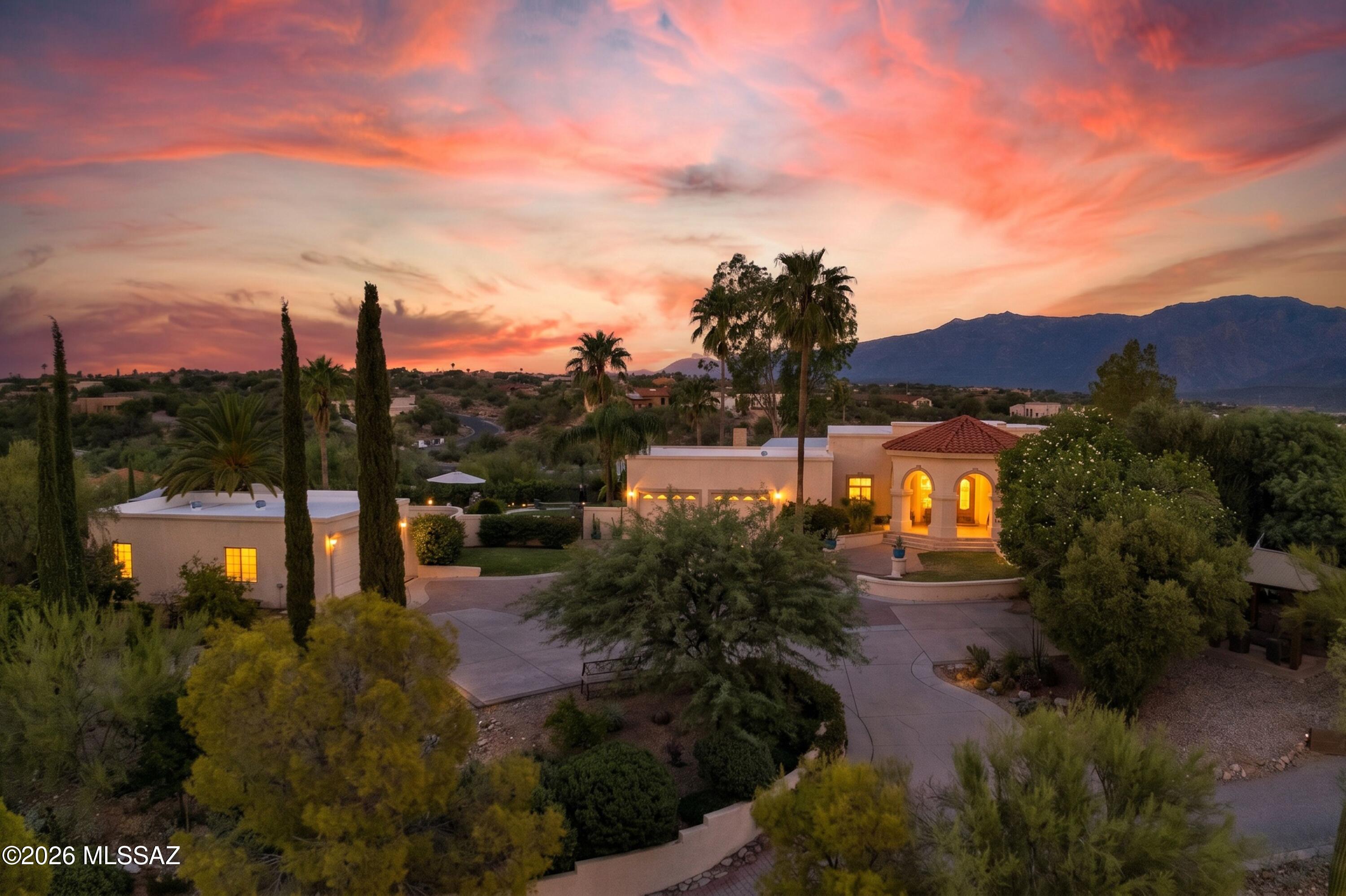 Perched on nearly two private acres with spectacular views of Pusch Ridge and the surrounding mountains, this exceptional hilltop estate offers nearly 4,500 square feet of thoughtfully designed living space, a private tennis court, resort-style outdoor amenities, and distinctive custom details throughout. The court provides a rare recreational amenity with exciting potential for tennis, pickleball, or a versatile multi-sport court, all within the privacy of your own estate. The gracious interior features three generously sized bedrooms, four bathrooms, and a handsome office/library. Expansive formal living and dining areas provide an elegant setting for entertaining, while the chef's kitchen is appointed with mostly newer luxury appliances. An impressive family room offers a (continued) fireplace, built-in bar, and direct access to the patio, effortlessly connecting indoor and outdoor living. Wood and travertine flooring extend throughout much of the home, complemented by newer upgraded carpeting in the bedrooms. The primary suite is a private retreat, capturing breathtaking mountain vistas from both the bedroom and its generous sitting area, an ideal setting to enjoy the changing desert light by day and sparkling city lights after sunset. Private balconies and patios throughout the residence offer additional opportunities to take in the remarkable surroundings. Designed for both recreation and entertaining, the outdoor spaces are exceptional. The private tennis court enjoys a dramatic mountain backdrop and offers the opportunity to create a personalized tennis, pickleball, or multi-sport experience. A spacious nearby gazebo overlooks the court and natural desert landscape, creating an inviting gathering spot for players and guests alike. An extensive covered patio, dramatic outdoor fireplace, and multiple seating areas provide wonderful spaces for year-round entertaining. The sparkling pool and spa are complemented by a designer outdoor shower and private pool bath, creating a resort-like setting at home. Mature landscaping and an abundance of fruit trees further enhance the property's distinctive desert character. Car enthusiasts, hobbyists, or those seeking exceptional storage will appreciate the oversized attached two-car garage plus a detached two-car garage with additional workshop or storage space. Two of the home's HVAC systems are newer, and the exterior is being freshly painted. With its elevated setting, extraordinary Pusch Ridge views, private tennis court, resort-style pool and spa, four-car garage capacity, and expansive indoor and outdoor entertaining spaces, this truly custom estate offers a rare combination of privacy, recreation, and sophisticated Tucson desert living.