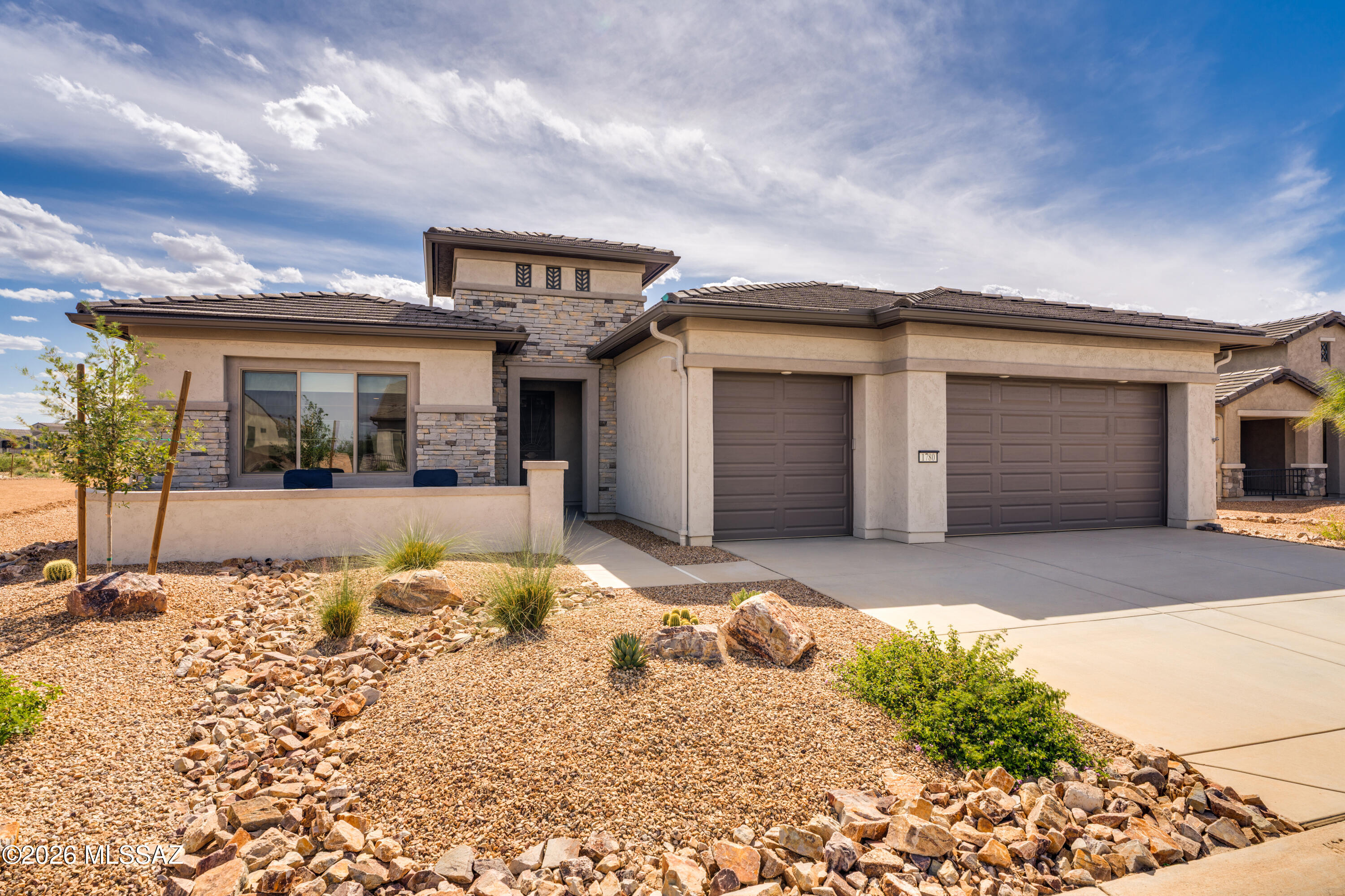 Less than 2 years new, this stunning 2024 Vienta model in Quail Creek is perfectly positioned on a premium lot backing to common area and walking paths, capturing scenic mountain views and breathtaking Arizona sunsets. Offering 2,353 sq. ft., this thoughtfully designed home features 2 BR, 2.5 BA, a versatile den, and a full 3-car extended-length garage. Impressive curb appeal with stacked stone façade and a welcoming front courtyard. Enter through a wrought iron security door into a bright foyer that opens to a spacious great room, complete with a stylish bar area and under-counter beverage cooler. The chef's kitchen boasts upgraded cabinetry with 41'' uppers, quartz countertops, tile backsplash, pantry closet, and a large island with apron sink, water purifier, and pendant lighting. LG stainless appliances include a 36" gas cooktop, vent hood, wall convection oven, and microwave. Interior features include luxury vinyl plank flooring in main areas, carpet in bedrooms, 8' doors and 5" baseboards throughout, and upgraded fans, lighting, and window treatments. The extended owner's suite captures mountain and sunset views, with a spa-like bath featuring dual vanity with undermount sinks, comfort height toilet, soaking tub, walk-in tile shower, and a large walk-in closet. A split bedroom design ensures privacy, with a guest bedroom offering its own en suite bath. The den with frosted glass French doors is ideal for an office, media or hobby room, or as an additional guest space, while a separate powder room provides added convenience for guests.  Laundry room includes extra cabinetry, utility sink, LG washer and gas dryer with pedestals, and an additional storage closet. Enjoy the extended outdoor living space with direct access to common area and walking paths--perfect for embracing the Arizona resort lifestyle.