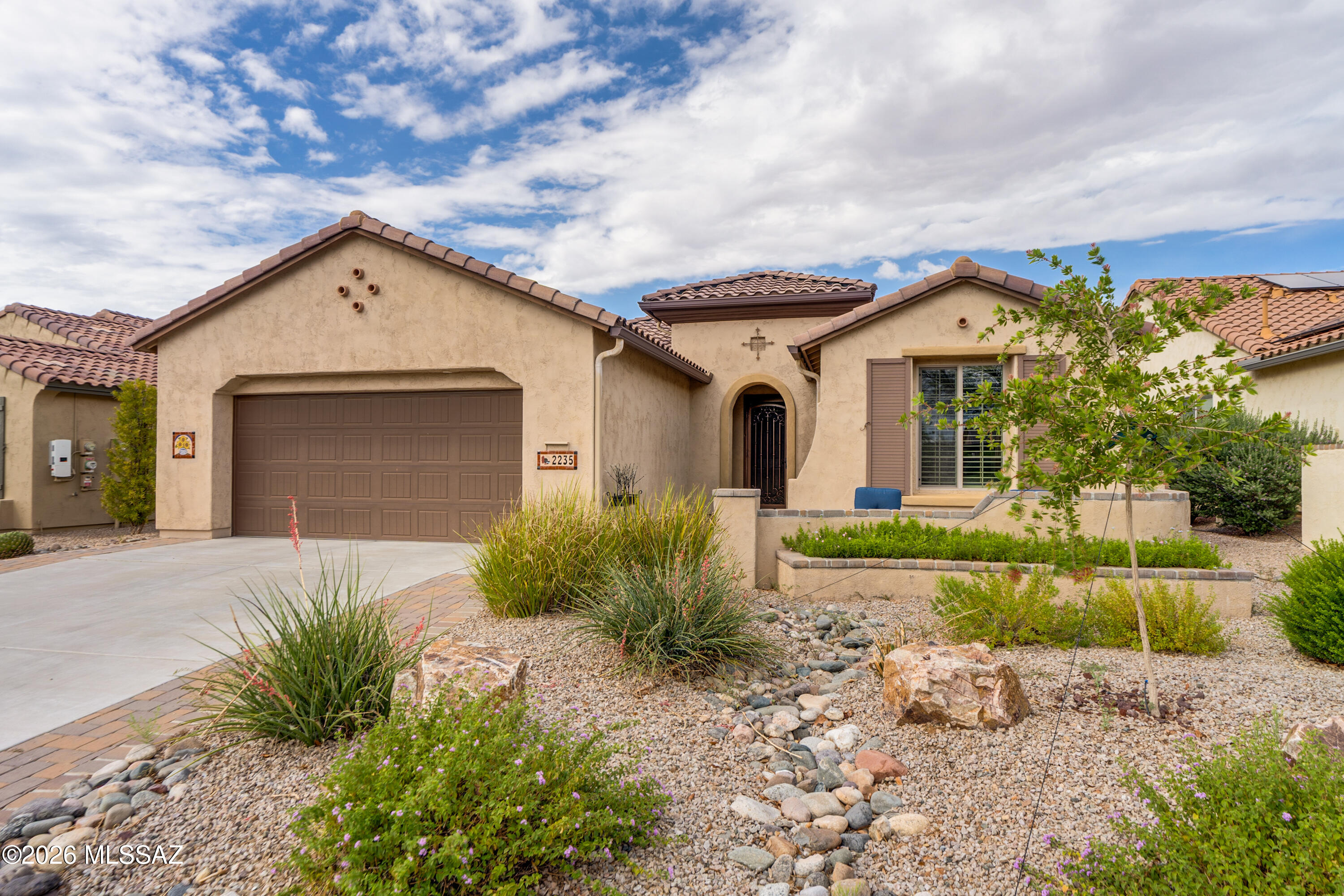 This well-appointed Fiesta model in Quail Creek resort community offers 1,994 sq. ft. of thoughtfully designed living space with 2 BR, 2.5 BA, and Den. Enjoy seamless indoor-outdoor living with a spacious front courtyard and a private rear yard backing to a lush common area. A wrought iron security door welcomes you into the foyer and spacious great room. The interior is enhanced by fresh paint, plantation shutters throughout, and Hunter Douglas top-down/bottom-up shades in the great room and den. The chef's kitchen features upgraded cabinetry, quartz countertops, tile backsplash, pull-out shelves, and stainless appliances including a gas range, wall oven, and microwave. A large island with breakfast bar, pendant lighting, trash pull-out, and single-bowl composite sink anchors the space. The adjacent dining area is extended an additional 2' for added comfort and larger gatherings. The extended owner's suite includes a bay window and a beautifully appointed bath with plank tile flooring, upgraded cabinetry, and a walk-in tile shower. A split bedroom layout provides privacy, with an en suite guest bedroom and a convenient powder room for visitors. The versatile den has french doors, ideal for a home office, media room, or additional sleeping space. Step outside to the covered rear patio and enjoy tranquil outdoor living with a water feature and scenic common area backdrop. Additional highlights include a recently updated laundry room with added cabinetry and counter space, rain gutters, a new irrigation system, and an extended-length garage with storage area and utility sink. This energy efficient home includes a solar lease with low monthly payments.