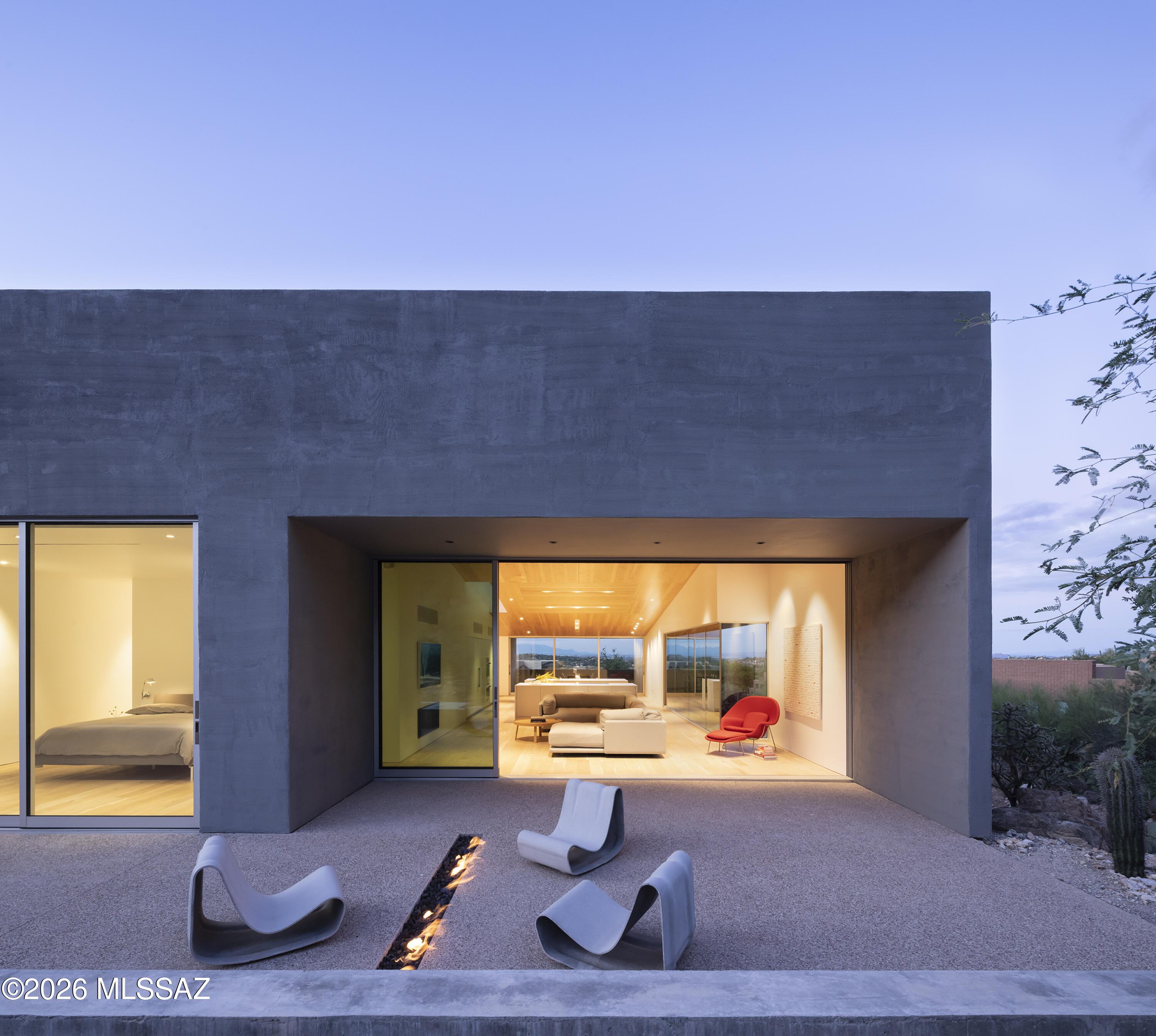 Ventana House rises from the sloping Sonoran Desert terrain, its forms grounded, sculpted, and elemental. Walls of textured material and deep apertures frame the landscape, mediating between exposure and refuge, allowing the desert to be experienced as a composed and measured extension of the architecture. Light, shadow, and space are orchestrated to reveal the environment slowly, with a sense of discovery around every corner. Designed by the renowned architectural firm HK Associates, the residence reflects the studio's disciplined approach to materiality, light, and form. The home has been featured in numerous international architectural publications, including Wallpaper Magazine, ArchDaily, dezeen, among others, underscoring its significance within contemporary desert modernism. The home unfolds as a sequence of calm, luminous spaces defined by precision and restraint. A double height entry gallery is washed in filtered daylight, while a perforated steel bridge introduces a moment of suspension before arriving at the primary living areas. Materiality throughout is refined and intentional. Plank hardwood floors extend beneath the matching wood ceilings, creating a cohesive warmth that contrasts with smooth painted walls and crisp white millwork. Mechanical elements, ventilation grilles, and lighting are recessed and aligned to preserve visual quiet.

The upper level accommodates the great room, a dedicated office, the primary suite, and a secondary suite, while terraces extend outward through expansive recessed glazing, softening transitions without overstating the connection. Living and dining spaces are situated beneath a sloped wood ceiling clad in wide plank boards that echo the contours of the foothills beyond. Integrated linear lighting and recessed fixtures are set flush within the ceiling plane, reinforcing continuity while modulating light throughout the day.

Kitchen and baths are articulated with slab front millwork, concealed hardware, and integrated monolithic surface countertops with precision edges and minimal shadow line reveals. In the primary bath, ribbed wall tile, large format flooring, frameless glass, and integrated surface vanities create a spa-like environment defined by texture and clarity.

The lower level is equally considered, housing an oversized three car garage, gym, office, den, laundry, and a third ensuite bedroom, each space composed to support both function and flow. Throughout, detailing is exacting, with tight tolerances and an emphasis on proportion and alignment.

Set within the guard gated enclave of Ventana Country Club, the home is complemented by access to world class club amenities and a network of nearby hiking trails that trace the foothills of the Catalina Mountains. These surroundings provide a natural counterpoint to the architecture without competing for attention, reinforcing a lifestyle that values both leisure and quiet immersion.

Ventana House is a modern desert retreat defined by clarity, restraint, and enduring craftsmanship - a residence where material integrity and architectural precision take precedence, allowing the landscape to be present, measured, and timeless.