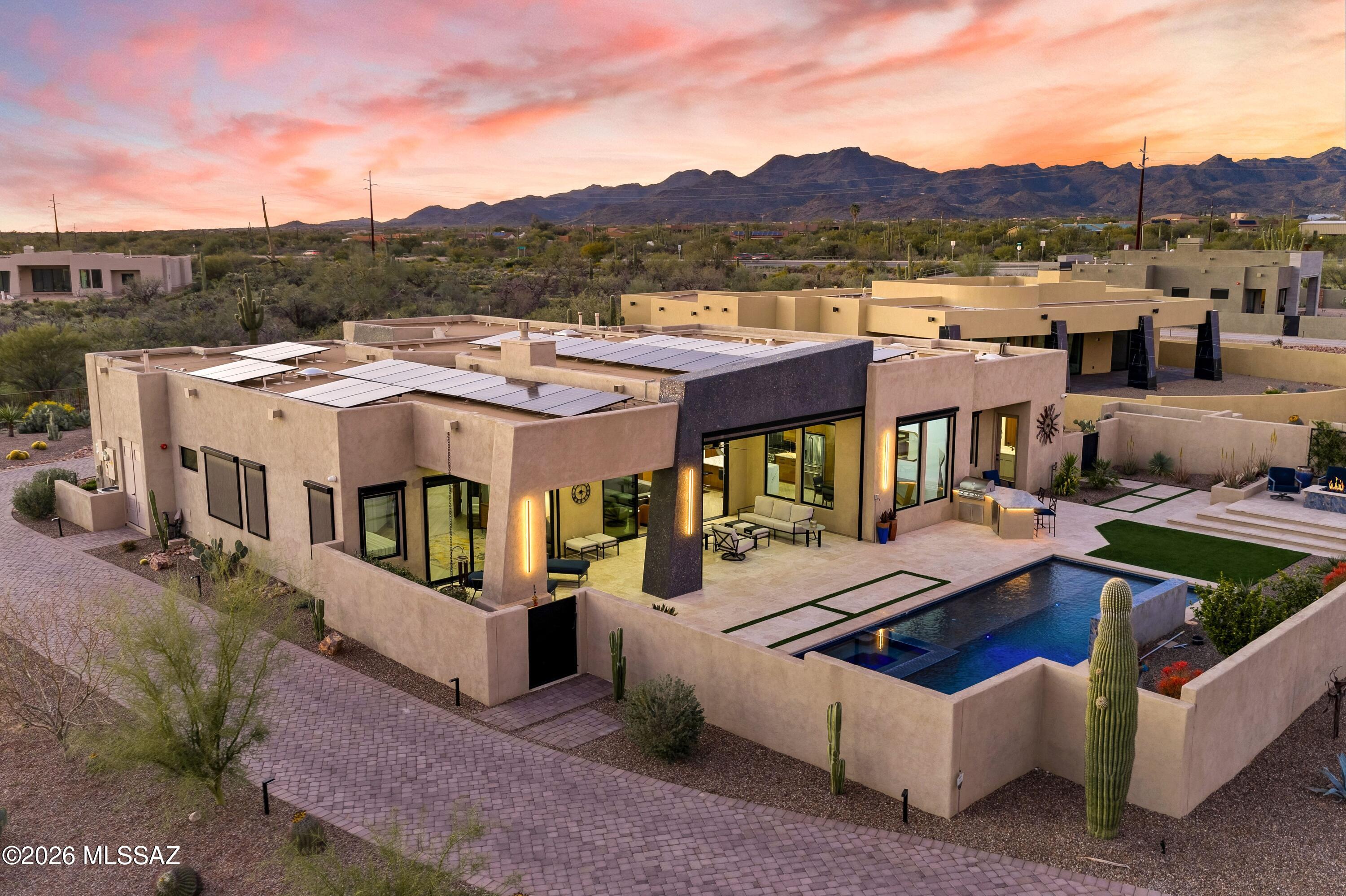 Perfection awaits at 11931 N Mesquite Sunset Place; a stunning property recently featured in Tucson Lifestyle Magazine. The vision of a custom home builder, interior design team and landscape architect have come together creating a brilliant experience indoors and out. The home is conveniently located in a small, gated enclave in Oro Valley. Built in 2023 and enhanced thereafter, you will find every bell and whistle imaginable. Leading to a private entry, the paver drive has been finished with low voltage lighting and thoughtfully placed desert plantings. Residents enjoy an angled oversized 3 bay garage for vehicles and storage, while guests are greeted by a calming fountain & stunning glass pivoting door. Situated with eastern and western exposure, the home is positioned to take in both sunrise and sunset, with views of multiple mountain ranges. 

Inside the 3,590 sq ft residence, high ceilings and light filled spaces are finished with high end windows, solid cherry doors, luxe quartz counters and custom cabinetry. A dramatic feature wall of gorgeous stone anchors the space and acts as a platform from which color is pulled into other spaces. Skylights are dotted throughout adding daytime illumination, while integrated lighting above soffits adds ambience at evening. Functionally designed with a split floor plan, the property offers 4 bedrooms, 3 ½ baths, plus a spacious den. Electronic blinds have been strategically placed both indoors and out to allow for light control, while maintaining views. Each bedroom has an ensuite or jack & jill bath, as well as a walk-in closet. Throughout, the condition is impeccable.

The indoors and outdoors unite with cascading sliding glass doors in both the great room and primary suite. With the help of multiple experts in outdoor design, the eastern facing backyard has been flawlessly finished. This space is truly an extension of the home. Flowing seamlessly, a spacious, covered patio with large format travertine extends to the heated saltwater pool and spa. The linear and modern pool was designed to include a water wall and an electric retractable cover.  An outdoor kitchen features a built-in grill, fridge, granite countertop and bar seating. Positioned for sunset views, an elevated seating area has been finished with a gas firepit and built in planters.

This is not just a beautiful home -- it's an intelligent one. The owners have incorporated a full-home security system, smart controls and hard-wired cameras. Two EV chargers are tucked neatly in the garage, which features its own climate-control system via a Samsung/Lennox mini-split and epoxy flooring. Solar panels on the roof, a whole-house water purification system and reverse osmosis drinking water underscore an emphasis on sustainability and attention to wellness.

This location in Oro Valley is ultra convenient. Immediately outside the gate, runners and cyclists enjoy access to The Loop multi-use paved trail system. Within 2 miles, there is a large grocery store, dining, shopping and the Oro Valley library. Within 10 minutes, you will find Oro Valley Hospital, Oro Valley Marketplace and Catalina State Park. An incredible lifestyle awaits.