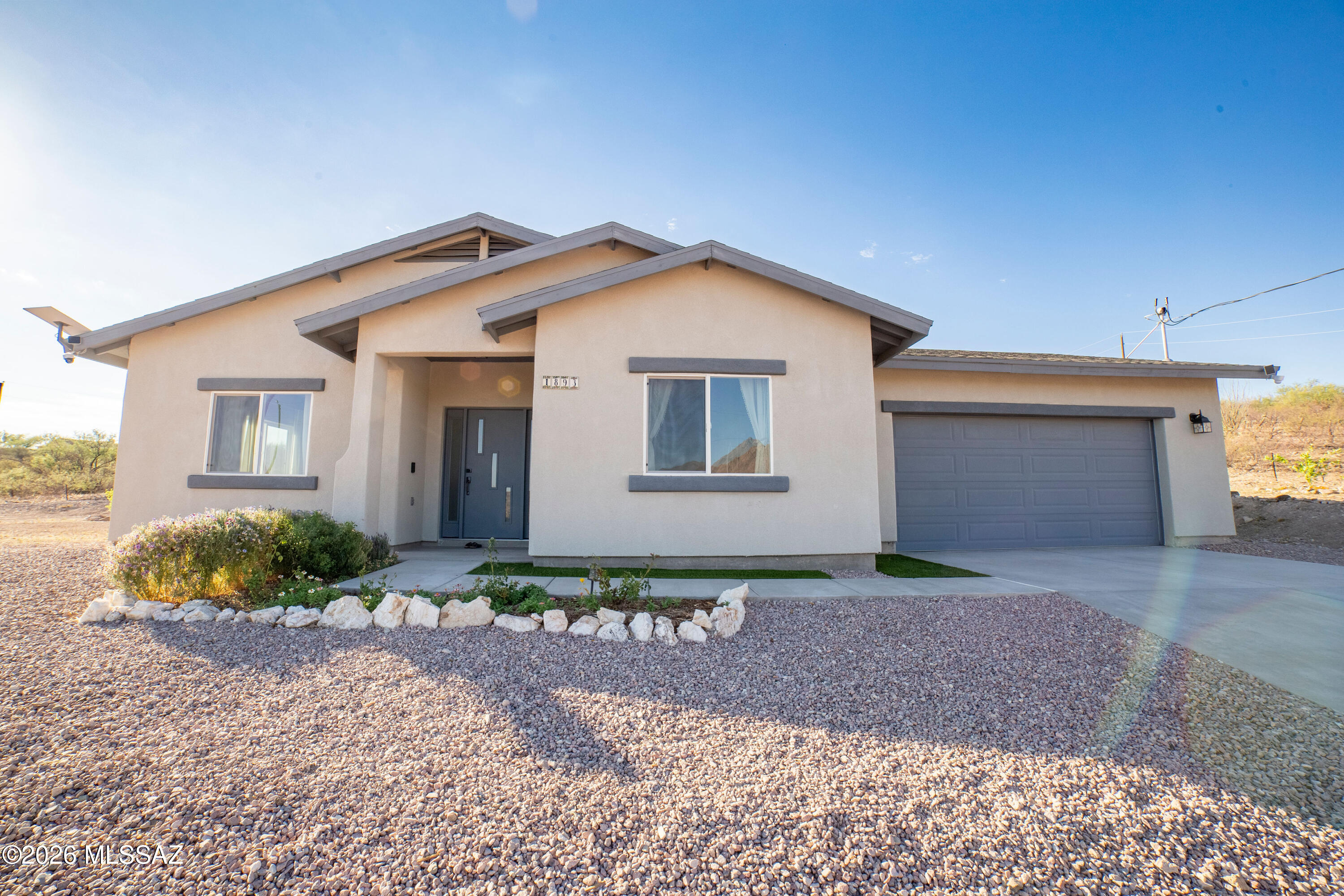 This beautiful new home welcomes you with stunning views of the Santa Rita Mountains and a bright, open layout designed for comfortable everyday living and easy entertaining. As you enter, the living room sits to the left, while the kitchen and dining area are thoughtfully positioned to the right, creating a warm and inviting flow through the main living space. Large windows throughout the home bring in natural light and showcase the mountain views from multiple rooms. The bedrooms are tucked down the hall, offering separation between the hosting areas and private living quarters. The garage features epoxy flooring, adding a clean and functional finish, with plenty of space for storage or hobbies. Additional features include security cameras, a water softener, and reverse osmosis system. Outside, enjoy a variety of fruit trees including apricot, apple, lemon, and two orange trees, along with mature ash and pine trees. Workout equipment may be available for purchase on a separate bill of sale.