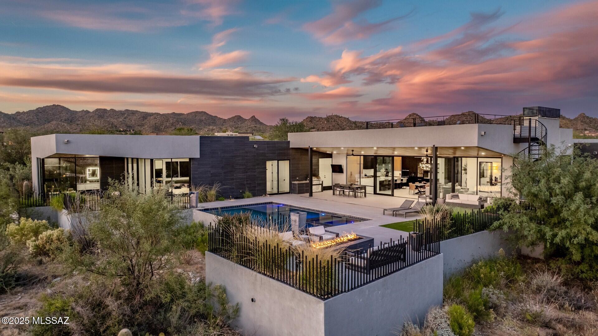 Modern luxury and integrated technology define this home, designed by renowned architect Marc Soloway with interiors by Designs by Priya. Located in Stone Canyon's premier guard-gated community, the property offers mountain views, unobstructed sunsets, and backs to preserved desert for privacy. A pivot front door opens to a streamlined floor plan with tall ceilings, 24x48 Italian tile, and a full glass wall overlooking the resort-style backyard. Western multi-slide doors create a true indoor-outdoor layout. The kitchen features a quartz waterfall island, Sub-Zero, Wolf, and Dacor appliances, a built-in Wolf coffee maker, dual sinks, a hidden walk-in pantry, white-oak accents, and a Sub-Zero wine column. T he primary suite includes floor-to-ceiling glass, a spa-inspired bath with black lavastone shower tile, floating vanities with LED mirrors, and a California Closets wardrobe. Secondary baths continue the same elevated detailing with floating vanities and full-height tile. The home is fully automated with a Control4 system managing audio, cameras, automatic shades, the cinema room, lighting, and more. Hallway lighting is upgraded to gallery-style fixtures. The cinema room includes built-in surround sound, an automatic projector, blackout shades, and a dedicated IT closet. Outdoor features include a saltwater pool and spa, view fencing, bar seating, and a Lynx Sedona grill. A custom metal spiral staircase leads to the rooftop deck for star-gazing, city light views, and sunset watching. A modern, well-built home with high-level finishes and a prime Stone Canyon setting.