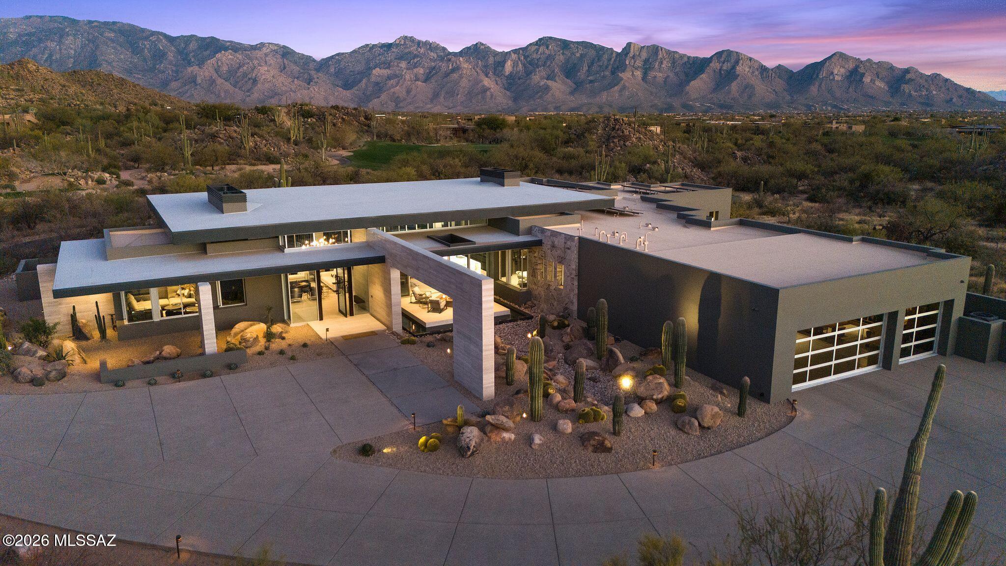 Fully turnkey and sold furnished as presented, The Reflectory is a luxury desert modern estate in guard-gated Stone Canyon, Oro Valley, Arizona - offering immediate enjoyment without the time or complexity of custom construction. Designed by acclaimed architect Ron Robinette, AIA, and built by The McHallam Company, this 5,247 sq ft single-level residence (built 2024) rests on 1.005 acres with panoramic Santa Catalina and Tortolita Mountain views. Commercial-grade steel frame and CMU construction, expansive Fleetwood glass walls, and imported Italian porcelain flooring establish enduring architectural integrity. Four en-suite bedrooms plus a lounge/den are supported by four full and two half baths. Custom German Eggersmann cabinetry anchors the kitchen, centered around a 14-foot underlit waterfall island and complemented by a Sub-Zero, Wolf, and Miele appliance suite within a three-zone culinary layout designed for both daily living and elevated entertaining. Indoor-outdoor living unfolds to a front reflecting pond terrace and rear infinity-edge pool and spa, outdoor kitchen, and glass viewing deck. All designer and collectible furnishings convey. Residents enjoy The Stone Canyon Club's private championship golf and fitness amenities, while Tucson's mild winters, Canyon Ranch, Miraval, and UNESCO culinary distinction frame a setting defined by light, space, and discretion - an exceptional backdrop for immediate ownership and the life you choose to step into here.