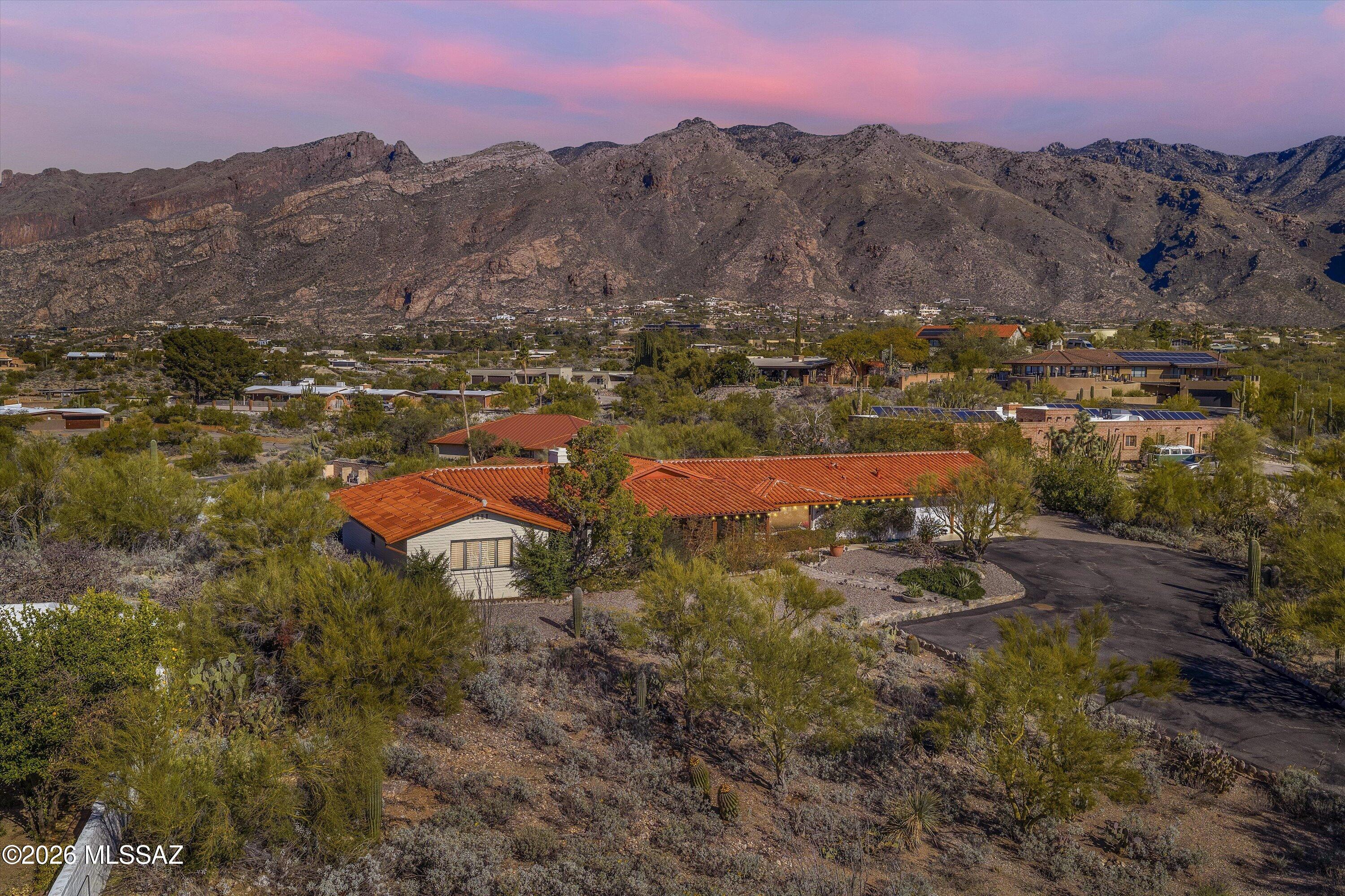 Perched on a coveted ridge in Skyline Bel Air Estates, this classic Catalina Foothills residence captures sweeping, unobstructed Catalina Mountain views and a sense of elevation that defines true Foothills living. Positioned noticeably above surrounding properties, the home enjoys panoramic sight lines, dramatic sunsets, and remarkable natural light throughout the day.
Built in 1968 with solid slump-block construction, the home reflects the enduring quality and authentic character that made the Foothills famous. These substantial walls provide natural thermal efficiency, durability, and timeless architectural appeal rarely found in newer construction.
Inside, approximately 2,869 square feet of thoughtfully designed living space includes expansive windows, generous living and dining areas ideal for entertaining, and comfortable separation between living and bedroom wings. Designed to capture the surrounding mountain scenery, the main living area offers generous scale and a layout that feels open and inviting. The spacious living room is highlighted by a fireplace, cathedral-style vaulted ceilings with exposed beams, and expansive windows that frame the Catalina Mountains while filling the space with natural light.
The kitchen offers abundant cabinetry, generous counter space, stainless appliances, and a practical layout that connects naturally to both casual and formal dining areas. An eat-in breakfast nook and built-in desk/workstation provide flexibility for everyday living, while the formal dining area enjoys views of the city, creating a memorable setting for gatherings and evening meals.
The bedroom wing provides separation and flexibility, including a spacious primary suite with mountain views, along with well-proportioned secondary bedrooms suitable for guests, family, or a home office.
Outdoor living is a highlight of the property. A kidney-shaped pool is positioned to capture the mountain backdrop, surrounded by expansive flagstone patios, multiple seating areas, and mature desert landscaping that blends seamlessly with the natural environment. Established saguaros, palo verde, and desert vegetation create texture, scale, and a sense of permanence that cannot be replicated in newer landscapes. A screened porch provides additional year-round outdoor living space ideal for morning coffee, evening gatherings, or enjoying Tucson's monsoon skies.
The property includes a two-car garage as well as a two-car carport, offering flexible covered parking and additional space for vehicles or guests.
Skyline Bel Air Estates is one of the Catalina Foothills' most established and desirable neighborhoods, known for its varied elevations, distinctive homes, and proximity to Tucson's best amenities. La Encantada's premier shopping and dining, world-class hiking in Sabino Canyon and Ventana Canyon, and the highly regarded Catalina Foothills School District are all just minutes away.
Ridge-top properties of this caliber rarely become available. With panoramic mountain views, authentic Foothills architecture, mature desert landscaping, and a setting defined by elevation and outlook, this home offers a rare opportunity to own a timeless piece of the Catalina Foothills lifestyle.