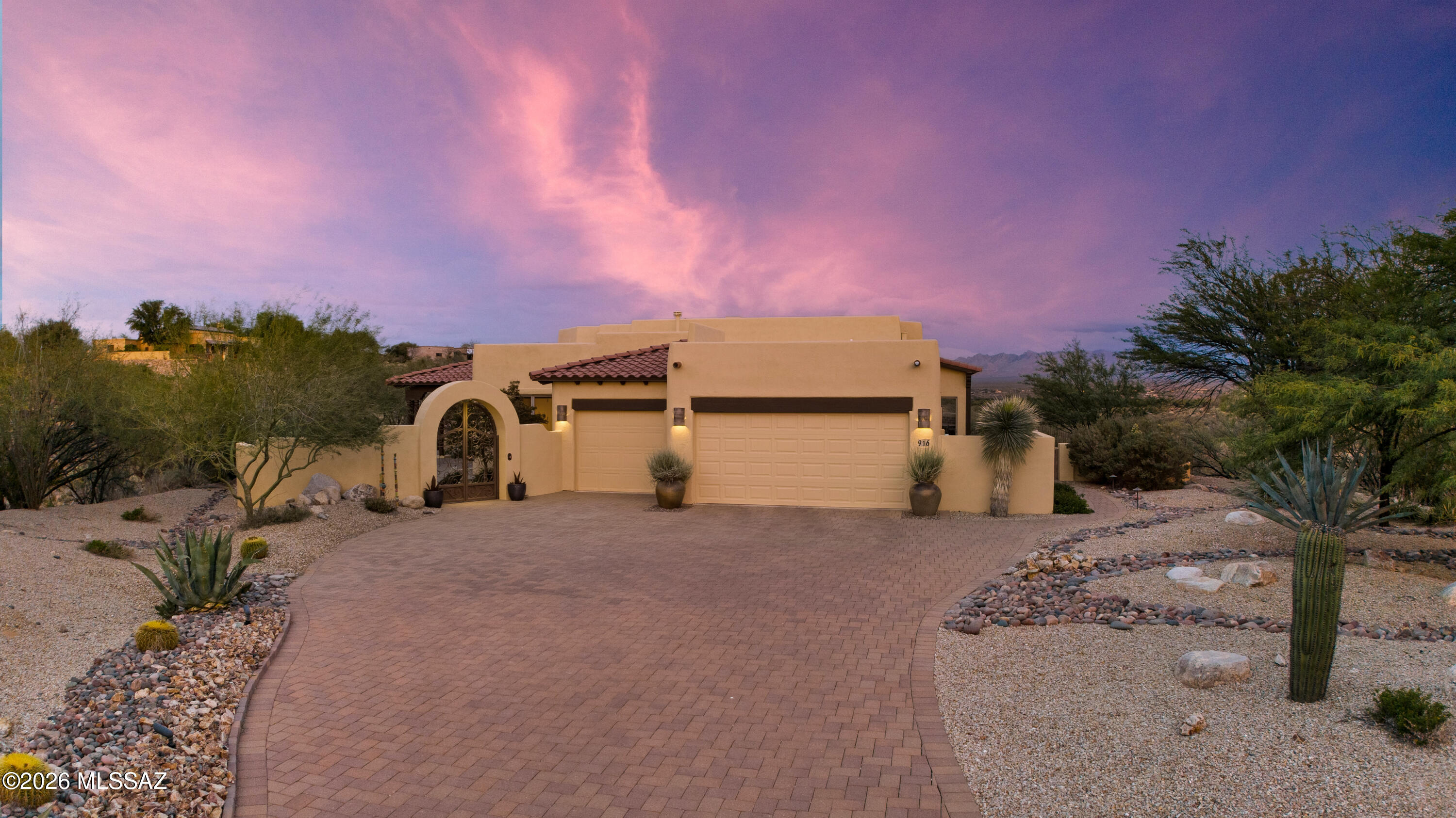 Nestled in the heart of Southern Arizona's magnificent high desert, this stunning estate offers an extraordinary canvas for the life you've been imagining—where every day feels like a celebration of natural beauty, cherished connections, and the art of gracious living. The property's dramatic setting is nothing short of breathtaking. Sitting high on a hill, sweeping vistas stretch endlessly across pristine desert landscapes, while the majestic Santa Rita Mountains paint an ever-changing backdrop of purples and golds. Deep arroyos carve through the terrain,  and the wide-open Arizona sky transforms from brilliant blue to star-studded black each evening. This home was designed for those who understand that life's best moments happen when we blur the boundaries between inside and out. The heart of the home is a magnificent great room with soaring ceilings, featuring  massive sliding doors that, when opened,  create a seamless, flowing space perfect for entertaining. Watch as your guests naturally drift between the climate-controlled comfort of the great room and the inviting outdoor living areas, conversations flowing as easily as the desert breeze.
The welcoming front courtyard sets the tone for your home's gracious hospitality, while the expansive rear patio becomes your private resort. Gather friends around the built-in fire pit for intimate evening conversations under the stars, or fire up the grill in the outdoor kitchen for unforgettable alfresco dining as the sun sets over the mountains. The kitchen stands as the culinary centerpiece you've always wanted, magnificent in both form and function, with a generous center island that naturally draws people in. Flow effortlessly from food preparation to the intimate breakfast nook for morning coffee, or host formal celebrations in the elegant dining area where mountain views become part of the table setting. Every meal becomes a special occasion in this thoughtfully designed space. The home's soaring ceilings create a sense of openness and light throughout, while distinct spaces offer opportunities for every aspect of life. Curl up in the cozy den, complete with its own fireplace for movie nights, tackle projects in comfort, or simply enjoy a quiet afternoon with a book. The grand primary suite is your personal retreat, overlooking the patio and views beyond, with a spa-like bath designed for relaxation and rejuvenation. A private guest suite with its own bath ensures visitors feel pampered and comfortable during their stay.  This impressive estate isn't just a house, it's an invitation to live with intention, beauty, and ease. Your next chapter begins here.