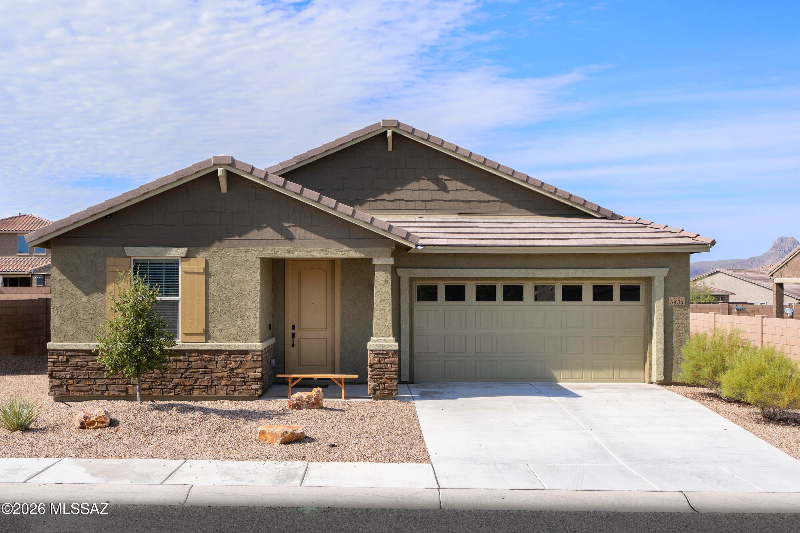Like new and ready to move in to now! This one-story Mattamy home in NW Tucson features an open concept floor plan with three bedrooms plus a bonus room, two baths and stylish design choices throughout. The 1736 square foot Emory plan has a Craftsman exterior elevation with a stone facade and offers common buffer space to the rear for privacy.  With tones of white, gray, cream and taupe throughout, the interior palette is suitable for virtually any décor style. Low maintenance wood-look tile runs through the living, dining, bonus room, kitchen, laundry and baths, while the bedrooms have neutral carpeting. The living space has a sliding glass door leading to the covered patio and private, fully fenced outdoor space. The kitchen is fully outfitted with all stainless-steel appliances, and th white Shaker-style cabinets perfectly complement the dark gray herringbone tile backsplash and the granite counters. An island with sink and breakfast bar anchors the space and is finished with chic café-style pendant lighting. The dining area with an industrial-style light is flanked by the open kitchen and living space and has built-in buffet base cabinets, perfect for party or dinner serving, while a double-door pantry adds even more storage. Rich gray accent walls in the living area and under the breakfast bar pull everything together and add drama to the space. The generous primary suite overlooks the backyard and has two walk-in closets and a large ceiling fan. An ensuite bath features a long vanity with dual undermount sinks, granite counters, a separate toilet room and beautiful, fully tiled walk-in shower with a built-in bench. Two guest bedrooms are serviced by a full hall bath with a granite-topped vanity, undermount sink and tub/shower combination. One of the guest bedrooms offers a feature wall in slick navy blue and a modern ceiling fan. A bonus room off the entry of the home would make a perfect home office, den or whatever else your lifestyle might need.  A conveniently located laundry room and a two-car garage round out this ultra-clean home. With the silhouette of mountains in the distance and common buffer space between you and your rear neighbor, the large, pool-sized backyard is a blank canvas for you to design your dream outdoor space. Your new neighborhood has lots of open space, a small park with green space and is located with quick access to Twin Peaks Road, the I-10 and Tucson Premium Outlets.