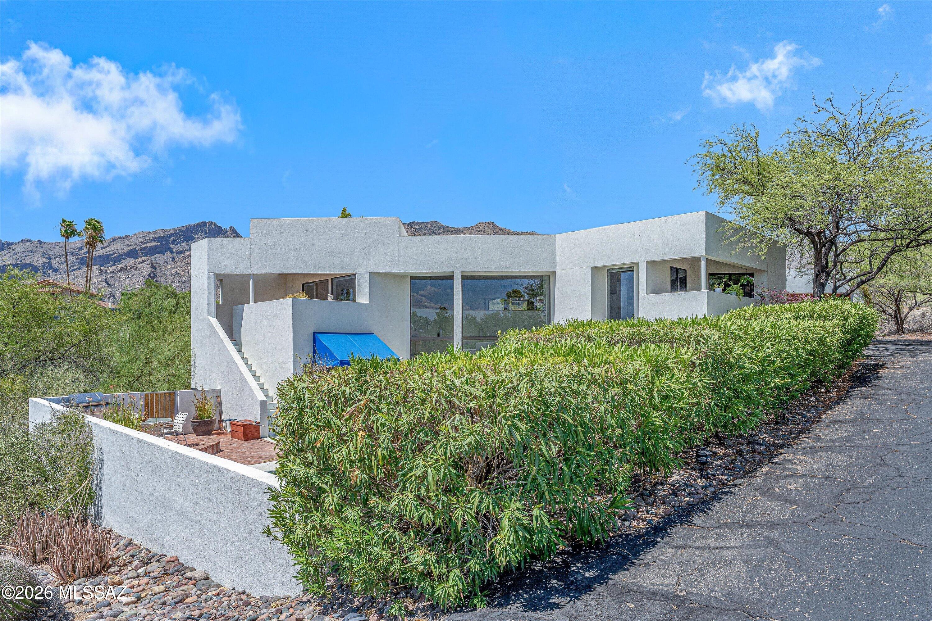 Designed by renowned University of Arizona Architecture Professor William Stamm, this architecturally significant two-story contemporary is a remarkable expression of desert modernism, privately situated on nearly an acre in coveted Skyline Bel Air Estates. Expansive floor-to-ceiling walls of glass capture breathtaking Catalina Mountain views, sparkling city lights, and the beauty of the surrounding Sonoran Desert. Offering approximately 3,528 square feet, this distinctive residence features 3 bedrooms, 3 bathrooms, dramatic living spaces, an upper-level terrace, resort-style pool, and detached casita. Stamm's visionary design blends timeless architecture with exceptional indoor-outdoor living, creating a home as captivating as its setting. 
Inside, rich oak hardwood and marble flooring create a beautiful balance of warmth and sophistication. The spacious family room opens directly to the covered patio and pool through expansive sliding glass walls, allowing the indoor and outdoor living areas to flow effortlessly together. Generous living spaces provide comfort and versatility for everyday living and entertaining, while track lighting throughout the main living areas offers flexibility for displaying artwork.
The kitchen features polished stone countertops, white cabinetry, and beautiful views overlooking the pool and natural desert landscape. Whether preparing meals or enjoying a quiet morning coffee, the surrounding scenery provides a peaceful backdrop.
The spacious primary suite offers a private retreat with a sitting room, walk-in closet, and generously sized full bathroom. Two additional bedrooms provide comfortable accommodations for family and guests. A dramatic great hall adds extraordinary versatility, offering possibilities for a media lounge, art gallery, billiards room, fitness studio, or additional entertaining space.
Upstairs, an inviting living room centered around a fireplace provides a comfortable gathering space, while the private upper-level terrace showcases panoramic Catalina Mountain views and dazzling city lights. From spectacular sunsets to the illuminated Tucson skyline, this elevated outdoor setting offers an exceptional place to relax or entertain.
The detached casita provides approximately 490 square feet of independently accessed flexible space, ideal for guests, a home office, or creative studio. The casita is not currently permitted as an ADU through Pima County. Buyers are encouraged to conduct their own due diligence regarding permitting eligibility, requirements, and allowable uses.
Outdoor living is equally impressive, with a resort-style pool, covered patio, and multiple areas to enjoy Tucson's beautiful climate. Set amid nearly an acre of natural Sonoran Desert landscape, the property offers exceptional privacy and frequent sightings of deer, bobcat, javelina, and an extraordinary variety of native birds.
The home's distinctive architectural character is reflected in Stamm's thoughtfully rotated floor plan, clean stucco forms, and striking flat roofline. Signature details, including the redwood garage door and cobalt awning, complement the contemporary design, while the expansive glass rear elevation creates a striking architectural presence.
Located within the highly acclaimed Catalina Foothills Unified School District and just minutes from La Encantada, premier dining, world-class golf, hiking trails, medical facilities, and Tucson's cultural attractions, this extraordinary property offers an exceptional combination of privacy, natural beauty, and everyday convenience in one of the Catalina Foothills' most desirable settings.