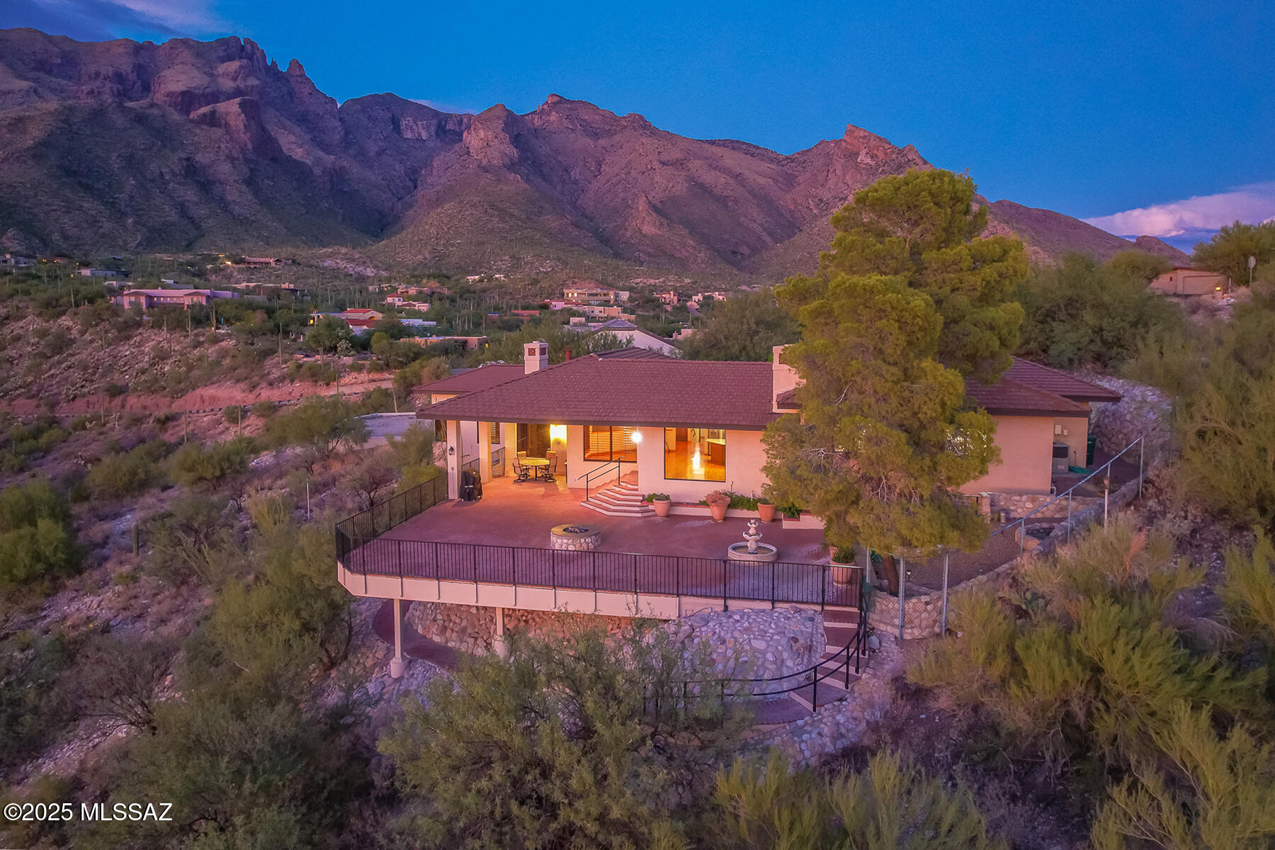 Nestled high in the prestigious gated Foothills II community, this 3,399 sq. ft. residence captures the essence of Tucson living with sweeping panoramic views of the mountains, city lights, and unforgettable sunsets. A private courtyard entry sets the tone for this warm and inviting home, where classic architectural elements blend seamlessly with dramatic natural surroundings. Inside, rich wood flooring flows throughout expansive living spaces highlighted by vaulted, beamed ceilings in the family room and bonus room. The main living room centers around a striking stone-faced gas fireplace framed by floor-to-ceiling windows that showcase breathtaking views. Two additional gas fireplaces add warmth and ambiance to both the family room and primary suite. The gourmet kitchen features granite countertops, stainless steel appliances, and an oversized center island, ideal for entertaining. Plantation shutters throughout the home enhance the timeless aesthetic while offering light control and privacy. The thoughtfully designed floor plan includes 3 bedrooms and 3 bathrooms, with a spacious primary suite offering a fireplace, dual walk-in closets, and a private office/den/bonus room, perfect for working from home or enjoying a peaceful retreat. Outdoor living is equally impressive: a massive paver back patio with a built-in fire pit overlooks the sparkling city lights below, creating the perfect setting for evening gatherings under the desert sky. With its unmatched views, elegant finishes, and premier location, this home offers an extraordinary opportunity to experience the beauty and serenity of the Tucson Foothills.