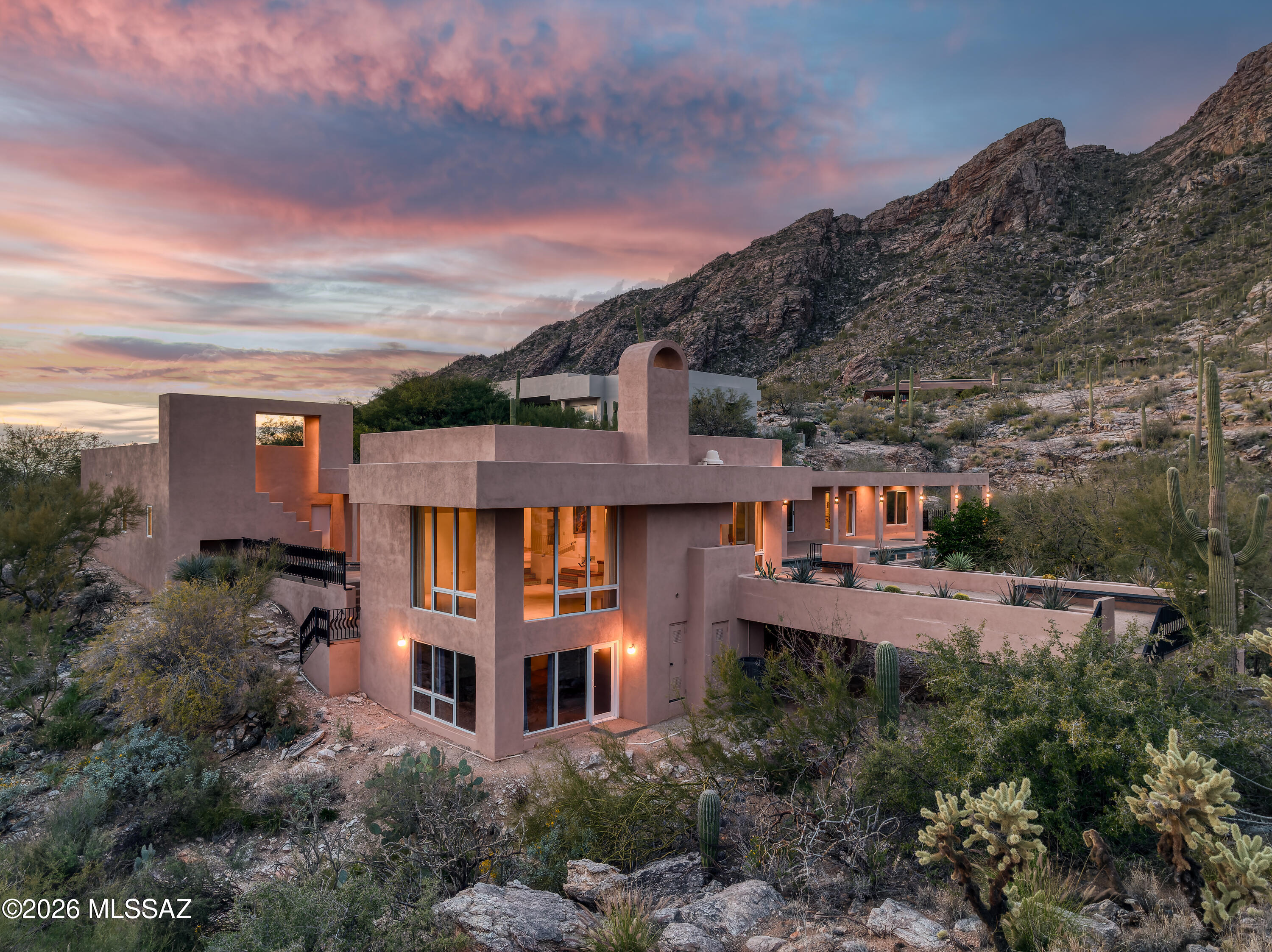 Set against a backdrop of protected mountain terrain in the highly sought-after Catalina Foothills, 7001 N Ina Place is a remarkable contemporary estate that embodies privacy, serenity, and elevated desert living. Located within an exclusive gated enclave of just ten residences, this property offers a rare level of quiet sophistication—where limited neighbors, expansive natural surroundings, and carefully preserved sightlines create an atmosphere that feels both secluded and refined. Spanning over 4,000 square feet, the home features 4 bedrooms and 4 bathrooms, thoughtfully designed to balance architectural drama with everyday livability. Expansive walls of glass frame incredible mountain and city views, allowing the vibrant colors of the Sonoran Desert to become part of the interior experience while filling the home with warm, natural light.

The surrounding desert landscape is nothing short of breathtaking. Majestic saguaros, native vegetation, and rugged rock formations provide a constantly changing canvas of color and texture, while the home's positioning against the mountains delivers extraordinary privacy rarely found in foothills properties. Here, the stillness of the desert, star-filled night skies, and the gentle sounds of nature create a tranquil retreat from the pace of city life.

Inside, the grand living spaces are both sophisticated and welcoming, ideal for refined entertaining or relaxed evenings at home. Custom built-ins showcase exceptional craftsmanship while adding both beauty and functionality throughout the residence. The seamless flow between spaces enhances the home's modern design and supports effortless gatherings.

The chef-inspired kitchen opens naturally to the main living areas, encouraging connection while maintaining a sense of understated luxury. Whether hosting elegant dinner parties or enjoying a quiet morning coffee with the mountains as your backdrop, the home is designed to elevate everyday moments.

The primary suite is a private sanctuary positioned to capture sweeping vistas while offering a peaceful escape. Generously sized secondary bedrooms provide comfort for family and guests, with flexibility for office space, fitness, or creative pursuits.

Outdoor living reaches resort caliber with a stunning 75-foot lap pool set against uninterrupted mountain privacy perfect for invigorating swims or relaxing afternoons beneath Arizona's endless blue skies. Beautifully curated patio gardens weave through the outdoor spaces, complemented by mature citrus trees that add charm, fragrance, and seasonal abundance.

The rooftop deck delivers a truly spectacular vantage point, where panoramic sunsets melt into glittering city lights and the Catalina Mountains rise in dramatic silhouette. It is an extraordinary setting for entertaining or quiet reflection alike.

Car collectors and hobbyists will appreciate the spacious 4-car tandem garage, offering ample room for vehicles, storage, or recreational equipment without compromising the home's sleek architectural presence.

Adding to the home's desirability is its placement within the highly regarded Catalina Foothills School District, known for academic excellence and strong community reputation an important consideration for those seeking both luxury and long-term value.

Despite its deeply private setting, the residence remains conveniently close to Tucson's premier dining, upscale shopping, golf courses, hiking trails, and cultural amenities. This rare combination of accessibility and seclusion further distinguishes the property.

7001 N Ina Place is more than a home, it is a secluded desert sanctuary where striking architecture, pristine landscape, and timeless views converge. Opportunities to own within such an intimate gated community, surrounded by natural beauty and enduring privacy, are exceptionally rare.