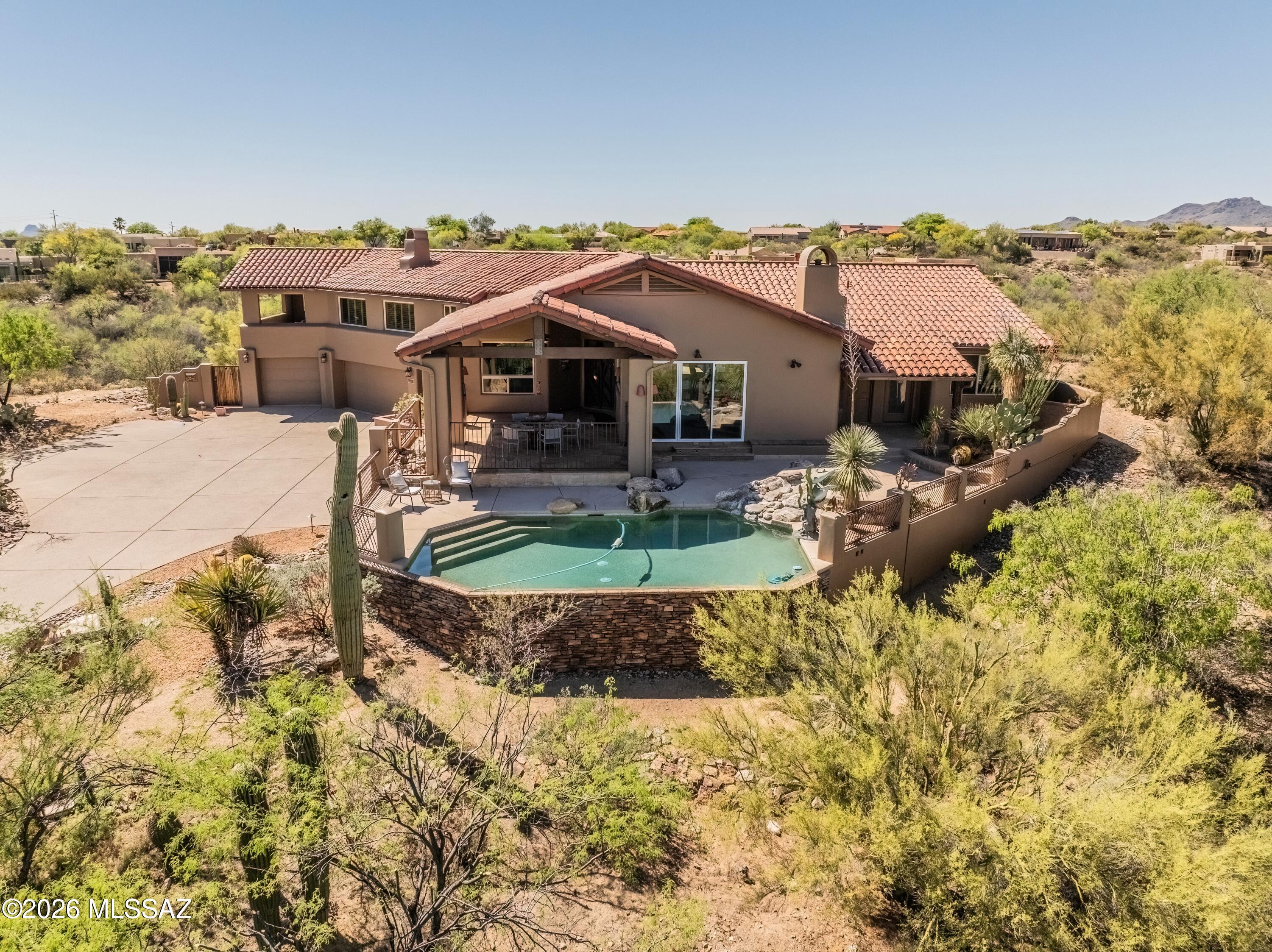 Perched high in the coveted Coyote Ridge enclave of Oro Valley, this extraordinary, gated estate captures the essence of elevated desert luxury. Privately tucked at the end of a cul-de-sac on a premier 1.2-acre ridge-top lot, the home is surrounded by sweeping, unobstructed views of the Catalina Mountains and Pusch Ridge offering a
level of serenity and privacy that is truly rare. Designed for both grand entertainment and refined everyday living, the outdoor experience is nothing short of spectacular. Multiple covered patios with rich wood beams and corbels frame expansive living spaces, while a custom-tiled built-in BBQ, outdoor shower, and a stunning negative-edge Pebble Tec pool with cascading rock waterfall and spa create a true resort-style retreat. From sun-drenched afternoons poolside to unforgettable Arizona sunsets and stargazing evenings, every moment here is elevated. Inside, the home exudes warmth and craftsmanship with wood like tile floors, solid knotty alder doors, and thoughtfully curated finishes throughout. The great room is both inviting and impressive, featuring soaring vaulted ceilings, a striking stacked-stone gas fireplace, and a dramatic wall of windows that perfectly frame the surrounding mountain vistas. The gourmet kitchen is
designed to impress, complete with stainless steel double ovens, a 5-burner gas cooktop, upgraded granite surfaces, custom cabinetry, and a seamless flow into the breakfast bar and dining area, each space thoughtfully positioned to capture
breathtaking views. The primary suite is a true retreat, offering a private sitting area with a dual-sided fireplace, direct patio access, and a spa-inspired bath featuring a jetted soaking tub, oversized tiled shower, executive-height granite vanities, and generous
walk-in closets. An adjoining flex space creates the perfect setting for a private office, fitness room, or relaxation lounge. The quality and attention to detail are evident at every turn in the home with fresh interior and exterior paint plus new plush carpet. The
home is both timeless and impeccably maintained. Backing to expansive preserved open space and offering unmatched privacy, breathtaking views, and exceptional craftsmanship this is a rare opportunity to own one of Oro Valley's most distinctive
luxury properties.