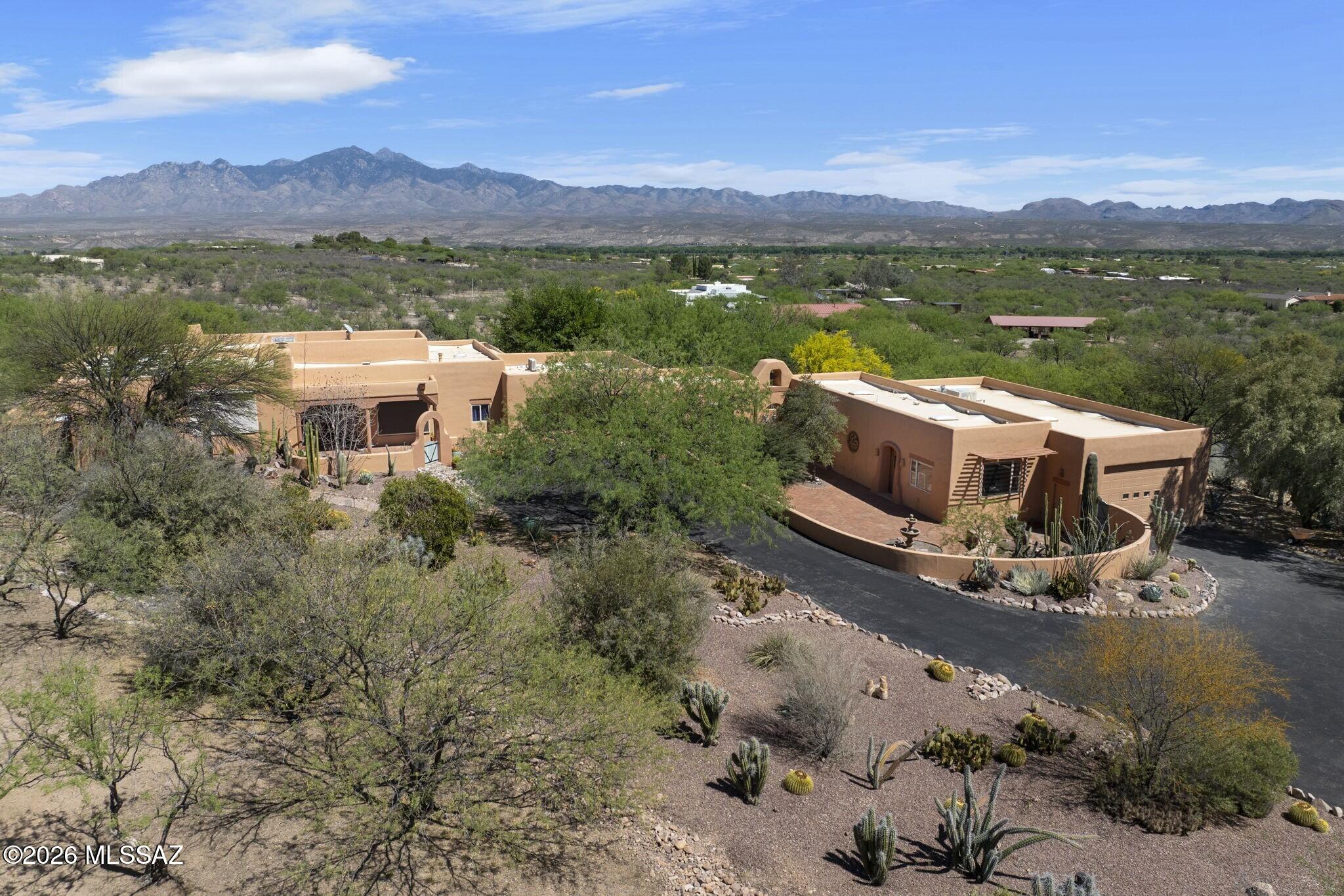 Located above the artists' and bird watchers' paradise of Tubac, Arizona, this southwestern-style home is set on 4.1 acres, enough for horses or other livestock.  The entire property is enclosed by a combination of an artistically welded steel fence (40%) and a closely positioned barbed-wire fence (60%) that excludes cattle and javelina.  A rolling steel gate encloses the driveway, and two additional steel gates provide access along the perimeter.  The home features expansive open-sky views of the Santa Rita Mountains to the east and the Tumacacori Mountains to the west. In the main residence, oversize windows in the living room, foyer, and kitchen overlook a veranda with outside dining and seating areas.  The west-facing dining room looks over the courtyard entrance to the home. The large beamed living room and primary bedroom in the main house feature kiva-style fireplaces, one gas and the other wood-burning.  A nearly wall-sized picture window in the primary bedroom allows viewing of the more than 70 species of birds that come to feeders.  A large walk-in closet is a feature of the primary bathroom.  Most large windows in the home have outside electric rolling shades.  A two-car garage attached to the main house contains built-in shelves that provide ample storage.  An enclosed courtyard with mature landscaping faces the Santa Rita Mountains and surrounds a pool, spa, and grilling station.  Much of the acreage outside the walled areas has mature trees and other desert plants.  An attached casita with a kitchenette and full bath offers privacy and flexibility for guests or multi-generational households.  An attached but separate building contains two large rooms and a half-bath that are currently used as offices and art/music studios but can be used as bedrooms.  A center room with numerous cabinets, drawers, and shelves has been used as a darkroom.  An expansive RV garage and workshop are major features of this building.