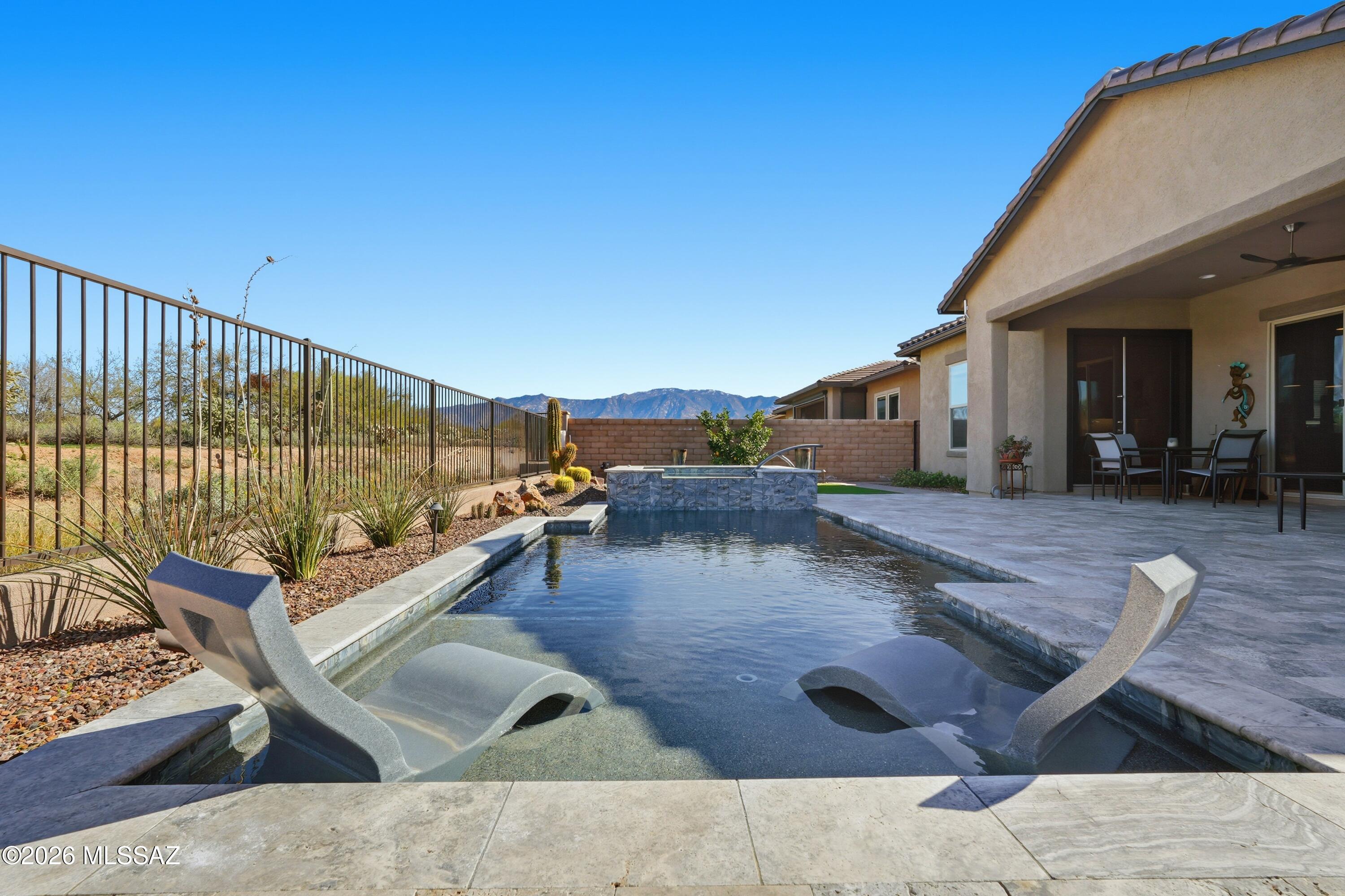 Set on a quiet street in a private gated community of only 39 Luxury-Level homes, all recently built, this handsome contemporary property includes over $280,000 in upgrades from the original model. A backyard oasis encompasses a gorgeous pool and spa with travertine decking that opens to the Vistoso Trails Nature Preserve, with miles of walking and biking paths and views of the Catalina Mountains. In the pool, enjoy a ''Beach'' landing for your lounge chairs and a self-cleaning system while taking in the tranquil mountain views. Handsome travertine pavers connect the well-sized covered patio and the pool area. The perfect spot to enjoy the sophisticated yet relaxed Oro Valley lifestyle! With a firepit nearby, it's an ideal setting for a delightful evening. Inside, the home radiates warmth with many upgraded features...custom barn doors, granite counters, French doors, soft close doors on cabinets...and plenty of space for relaxed living. Kitchen features custom pull out drawers. The kitchen offers ample storage in cabinets and a large walk-in pantry, along with a generous island and breakfast bar with attractive pendant lighting. An adjacent butler's pantry provides additional storage, counter space, and a GE Monogram wine cooler, adding to the home's ease of entertaining friends and family. The great room opens to the bountiful outdoor area and affords a cozy indoor spot to view the neighborhood wildlife of rabbits, deer, and bobcats that live nearby. A dining area provides vistas of the desert in the Preserve, and French doors to the outdoors. A separate dining room is utilized as a den, and could be an elegant setting for formal dinners with the addition of a fabulous chandelier.
Four bedrooms and three full baths ensure that there is space for everyone, whether family or visitors. The primary bedroom overlooks the pool and encompasses a bath with granite counters and double vanities and a fabulous walk-in shower accompanied by a versatile walk-in closet. Three additional bedrooms and two baths complete the living ensemble. A three car garage is attractively finished with an epoxy coating, ensuring ease of cleaning. 
In this handsome Oro Valley home, refined living combines with an extraordinary setting to provide an opportunity for an elevated living experience in sought-after Rancho Vistoso.