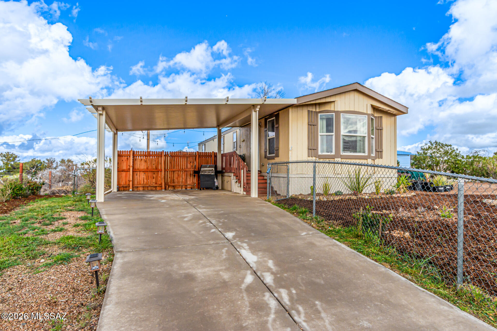 Seize the chance to own this charming 2-bedroom manufactured home on a fully-fenced lot. You're welcomed by a spacious front yard, an attached carport, and breathtaking views. The serene living room features vaulted ceilings, a soothing palette, a lovely bay window, and durable tile flooring. Cook delicious meals in the eat-in kitchen, equipped with ample wood cabinetry with crown moulding, contemporary track lighting, essential built-in appliances, and a convenient peninsula with a breakfast bar for quick meals. The main bedroom includes a private bathroom with dual sinks for an efficient daily routine. Outside, the sizeable backyard includes pristine artificial turf, sheds for additional storage, and a garden area. Don't miss out on this fantastic opportunity!