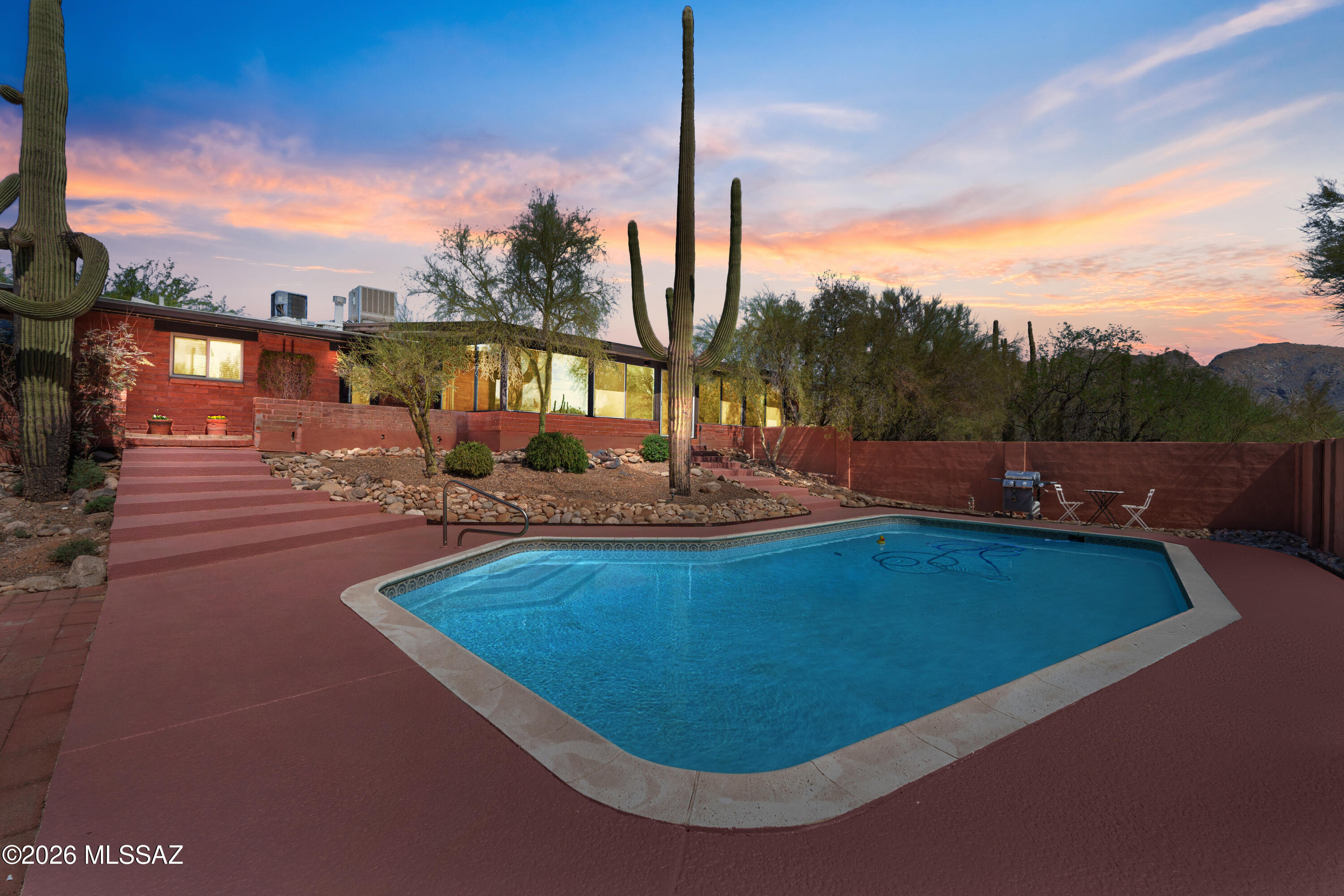 Classic mid-century modern architecture meets thoughtful, high-end reimagination in this exceptional 1963 adobe set on a private .88-acre lot in the Catalina Foothills. With 4 bedrooms, 3 bathrooms, and 2,779 square feet, the home has been meticulously updated while honoring the clean lines and warmth of true MCM design. An understated exterior gives way to beautifully carved double wood doors, clerestory windows, and light-filled interiors. The inviting living room is anchored by a striking masonry wood-burning fireplace that contrasts perfectly with the home's architectural simplicity and flows seamlessly into the main living spaces. The kitchen is a true focal point, featuring custom exotic wood cabinetry crafted from a single tree specimen, white quartz countertops, and a waterfall-edge bar. A breakfast nook with pass-through window and views of the family room, backyard, and pool keeps the space open and connected, ideal for entertaining. The converted Arizona room offers year-round enjoyment with views of downtown Tucson and A Mountain. New dual-pane windows, a sliding glass door, and a whisper-quiet mini-split create a comfortable space for morning coffee, evening dining, and relaxed gatherings. Three guest bedrooms are thoughtfully arranged along the hallway, along with a beautifully updated bathroom that functions as a pool-ready wet room with direct backyard access and interior laundry. The primary suite is a serene retreat with backyard and pool access and a stylishly updated primary bath. Every detail has been carefully curated to preserve the home's mid-century soul while delivering modern comfort and timeless appeal. A rare Catalina Foothills offering.