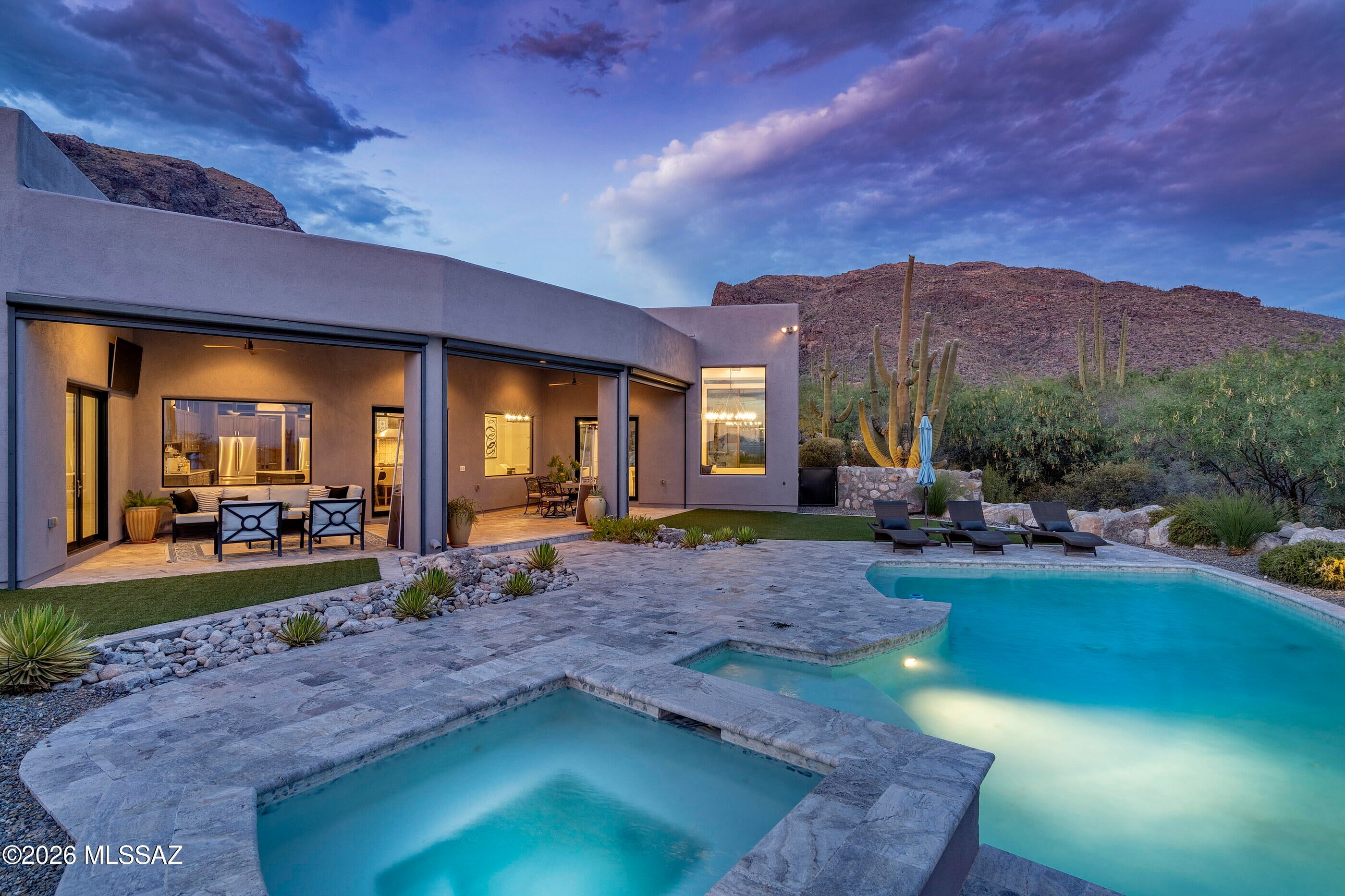 Designed by renowned architect Kevin Howard and completed in 2018, this exceptional contemporary residence is privately situated on a 1.25-acre homesite within the secondary gates of Pima Canyon, one of Tucson's most sought-after guard-gated communities. Framed by sweeping Catalina Mountain views and surrounded by mature saguaros and native desert landscape, the property offers a rare combination of architectural significance, privacy, and modern luxury.

Spanning approximately 5,805 square feet, the single-level floor plan features five ensuite bedrooms, expansive living spaces, soaring 16-foot ceilings, and walls of glass that capture the surrounding mountain vistas while filling the home with natural light. A dramatic Victory Metal Works iron and glass entry door establishes an immediate connection to the desert setting and introduces the home's sophisticated contemporary design.

The formal living and dining rooms were designed for both everyday living and refined entertaining, anchored by a striking floor-to-ceiling porcelain tile fireplace. Large-format porcelain flooring, exposed wood beams, motorized window coverings, and 8-foot alder doors throughout reflect the home's exceptional level of craftsmanship and attention to detail.

At the heart of the residence, the chef's kitchen combines functionality with designer finishes. Custom cabinetry offers extensive storage and organization, complemented by Calcutta and Fossil Gray quartz countertops, a Marrakesh porcelain tile backsplash, a fireclay apron-front sink, oversized center island, and a spacious walk-in pantry. Premium Bertazzoni Professional Series appliances include a 48-inch six-burner gas range and dual 36-inch French door refrigerator/freezer, creating an ideal environment for both casual meals and large-scale entertaining.

The primary suite serves as a private retreat, distinguished by rich hickory plank flooring, exposed wood beam ceilings, a secluded patio overlooking the desert landscape and Catalina Mountains, and a spa-inspired bath finished with floor-to-ceiling marble surfaces. Additional features include a freestanding soaking tub, walk-in shower with multiple shower heads, dual vanities with Cashmere Carrera quartz countertops, a dedicated makeup vanity, and a spacious walk-in closet with integrated washer and dryer. Four additional ensuite guest bedrooms provide exceptional accommodations for family and visitors.

Outdoor living is equally impressive. The resort-style backyard was thoughtfully designed to embrace Tucson's year-round climate, featuring expansive patios, multiple lounging areas, a sparkling pool and spa with spillway, professionally designed desert landscaping, natural boulder accents, artificial turf, and unobstructed Catalina Mountain views. Remote controlled sun screens enhance comfort throughout the outdoor living areas, creating inviting spaces for both relaxation and entertaining.

A consistent commitment to care and maintenance is evident throughout the residence. Three Trane HVAC systems service the home, providing efficient, zoned climate control, complemented by an owned solar photovoltaic system that enhances long-term energy efficiency. Additional highlights include a 1,493-square-foot four-car garage with extensive built-in cabinetry, a brick cobblestone driveway, and exterior enhancements such as repainting and a full roof re-coating completed in September 2025.

Combining award-winning architecture, contemporary design, premium construction, and breathtaking Catalina Mountain views, this remarkable Pima Canyon residence represents a rare opportunity within one of Southern Arizona's premier luxury communities.