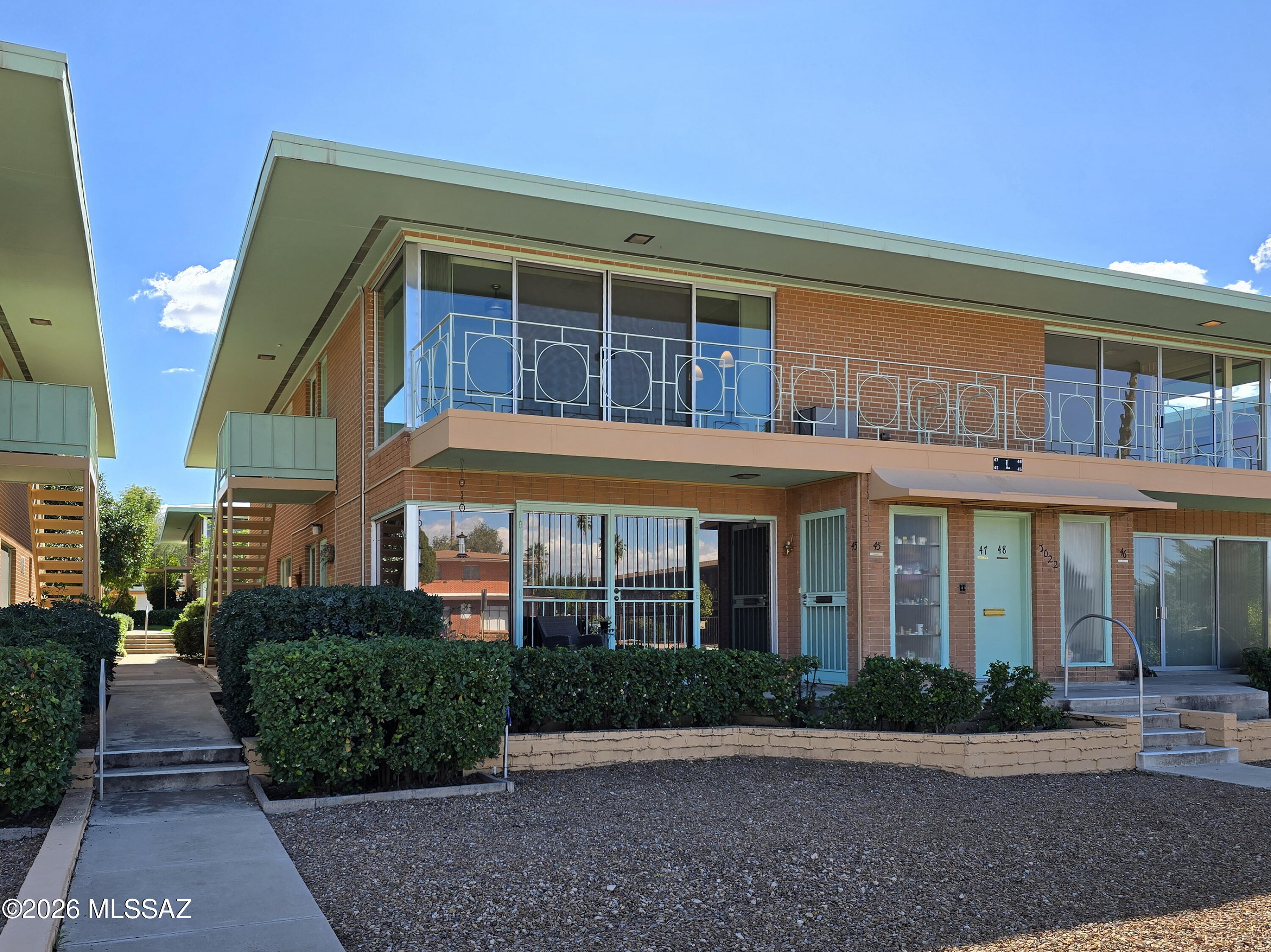Are you ready for some serious ''Mad Men'' vibes? Located in the Sam Hughes neighborhood, Villa Catalina is the only mid-century modern 55+ community listed in the Tucson National Historic Registry and offers a living experience that you simply can't find elsewhere in Tucson. 
This upper level unit has two convenient entry points--an interior entry that opens into the living space (and offers a stairlift for accessibility) and an exterior steel staircase that leads directly into the kitchen. Featuring two bedrooms and two baths, this 1409 square foot condo still has many of its original elements, affording the new owners the option to keep a vintage look or remodel into a more ''today'' aesthetic. The large, open living space with a balcony offers expansive windows to the front and side showcasing the hustle and bustle of the street below against the backdrop of the Catalina Mountains.  Flooded with natural light, this room has many options for furniture arrangement and a built-in display cabinet with accent lighting. 
The efficient kitchen is darling and features a clever flip-up table that's perfect for a quick meal or extra workspace. Maintaining its MCM look but balanced with modern conveniences, the kitchen offers a vibrant aqua blue tile backsplash, a matching vintage oven, dishwasher, microwave, modern electric cooktop, fridge and white quartz counters.  The large primary bedroom is at the rear of the unit, offering its own full bath, private balcony and a wall length pass-thru closet. This room's balcony offers new owners a wonderful spot for pleasurable birdsong filled mornings and overlooks a canopy of mature citrus trees.  A generously sized second bedroom has built-in shelving and storage, making an ideal study or guest room. This bedroom is serviced by a hall bath that still has its "Mamie Pink" shower, counter and backsplash tiles as well as the original cabinetry with an apron sink. No need for the laundromat--there is a "grandfathered in" laundry closet with a stackable washer/dryer in the unit.  The lush common areas are beautifully maintained, boasting mature trees and other plantings. This complex also features two pools, shuffleboard courts and a putting green. Your new home also includes one car space in a shared garage. Centrally located, close to shopping/dining and just moments from the University of Arizona, Banner Medical Center and El Con Shopping Center, this condo is also under ten minutes by car to the iconic Tucson Botanical Gardens and Reid Park Zoo.