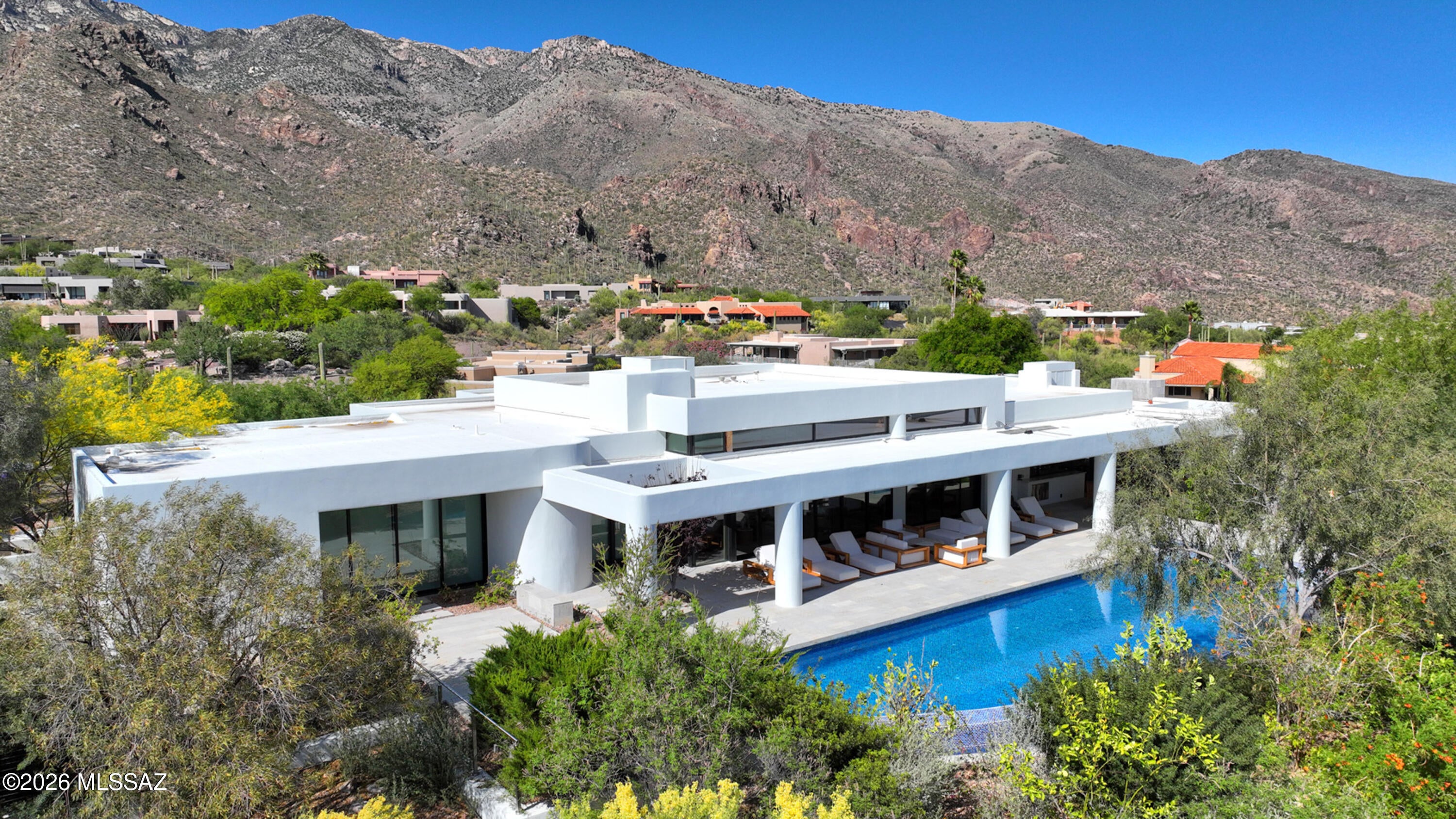 Set high in gated Finisterra, Terra Grande brings sculptural contemporary architecture into conversation with sweeping mountain, desert and city-light views. A circular drive leads to a stone-accented entrance, where expansive glass, warm wood tones and generous living spaces create a home equally suited to quiet mornings and memorable evenings with guests.
The kitchen anchors the home with sleek cabinetry, a substantial island, four ovens and a wine refrigerator. Thoughtfully appointed baths feature Carrara marble showers, ROHL fixtures, slipper tubs and TOTO toilets, bringing material richness to the home's clean architectural lines.
Deep covered terraces open toward an infinity-edge pool and spa, while an outdoor kitchen sets the scene for dinner overlooking the valley. Separate guest accommodations offer privacy for extended stays, and a sauna provides a welcome place to unwind. With five garage spaces and a 1.42-acre setting, Terra Grande combines a distinctive architectural presence with the comfort and flexibility of a private foothills retreat.